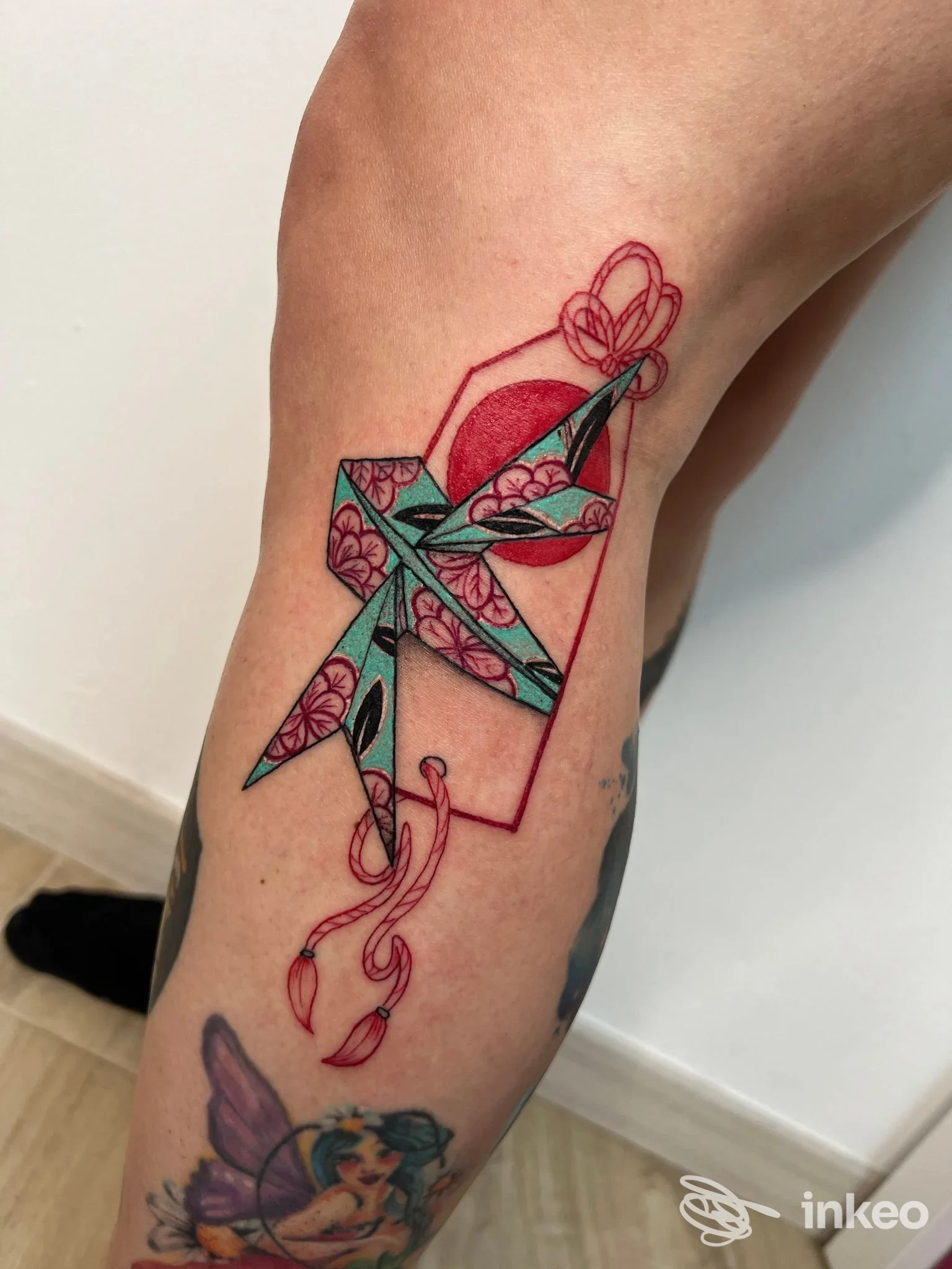 Tatuaggio geometrico con fiori sull’avambraccio, realizzato da Wip Tattoo a Piacenza, con linee rosse e riempimenti colorati.