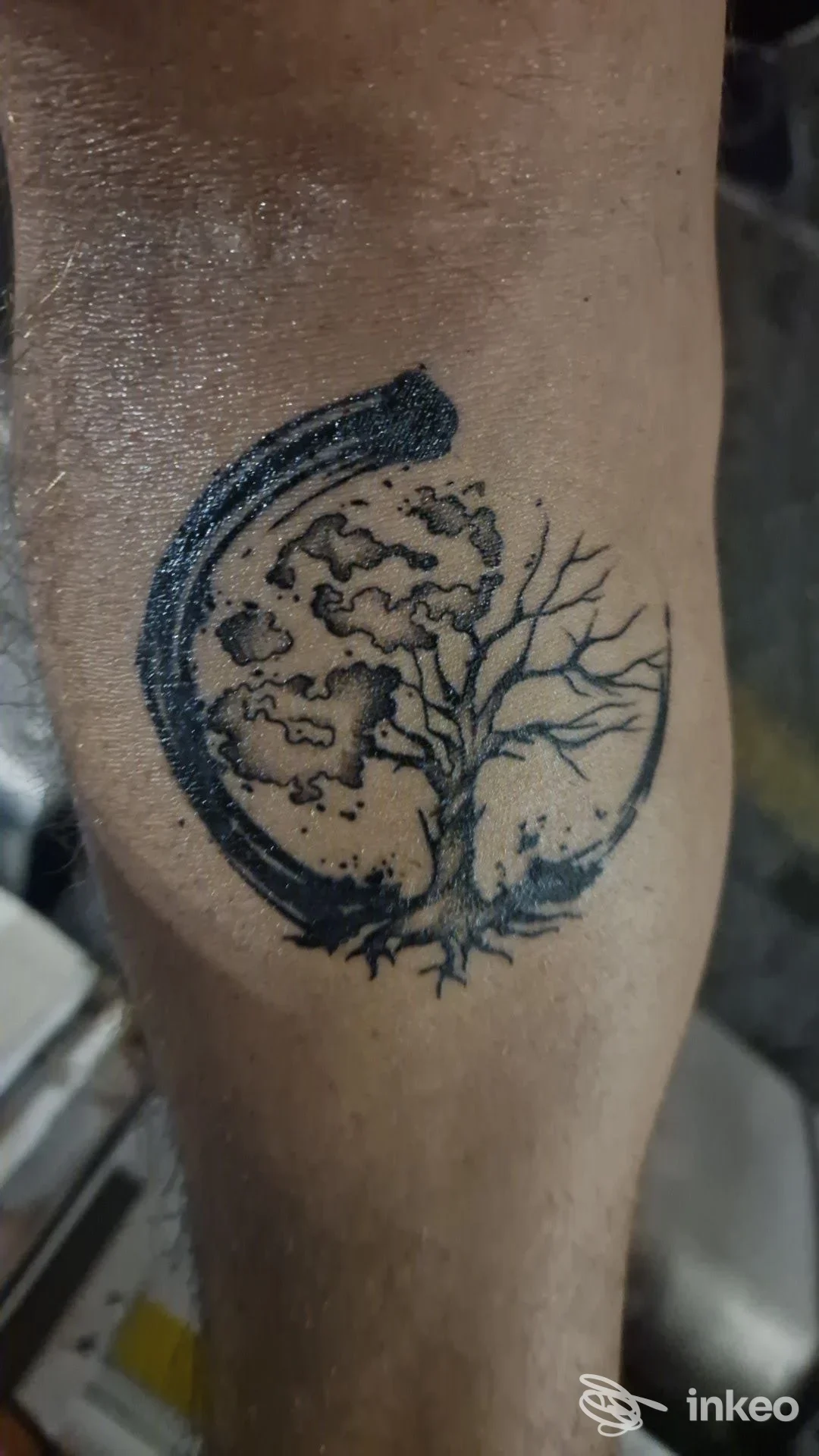 Tattoo sul polpaccio raffigurante una luna e un albero, contorni scuri e dettagli sottili, senza altre parti visive o testo.