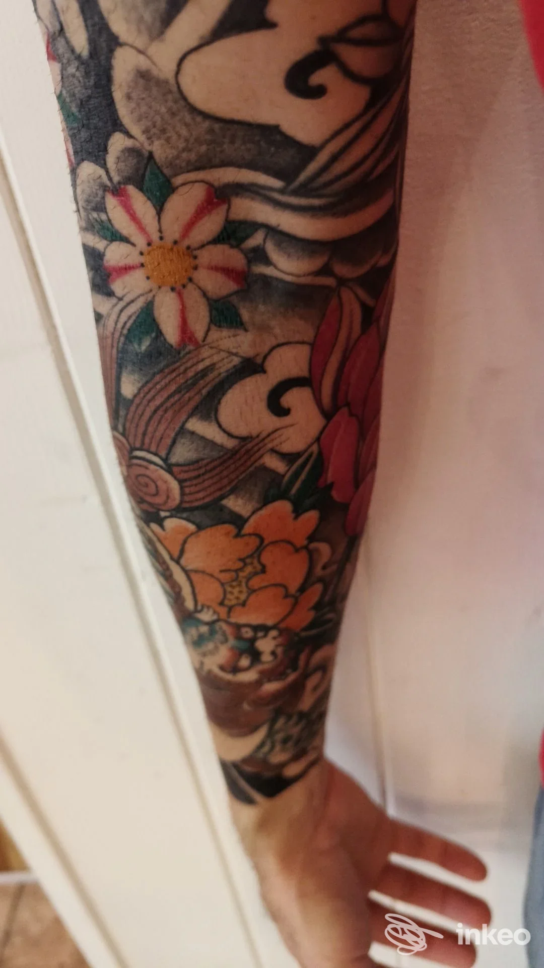 Tattoo a manica su gamba con fiori colorati e linee nere spesse, visibile pelle e dettagli del disegno.