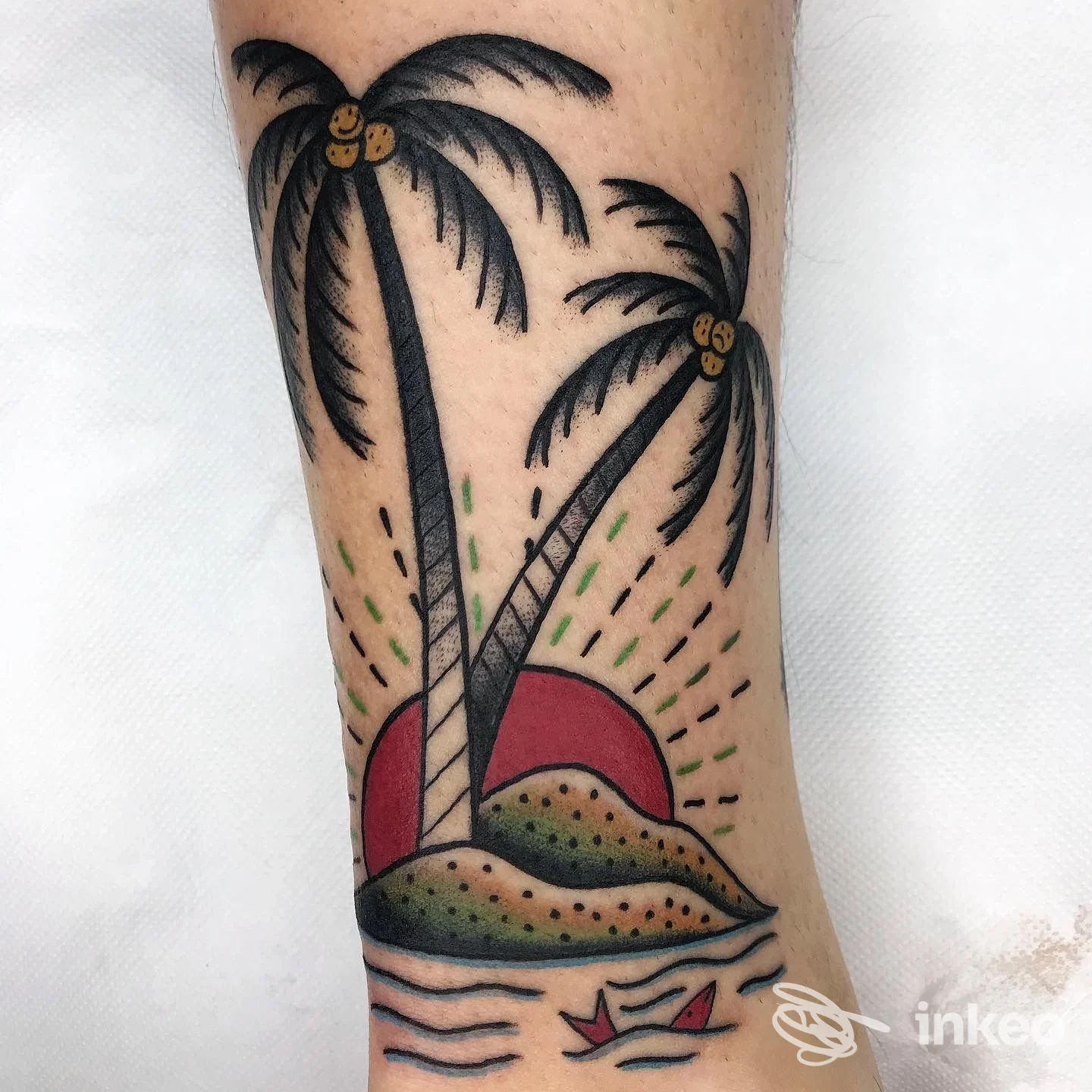 Tattoo a palme su avambraccio con tramonto, onde e sabbia; colori neri, rosso e verde; stile tradizionale, braccio visibile senza volto.