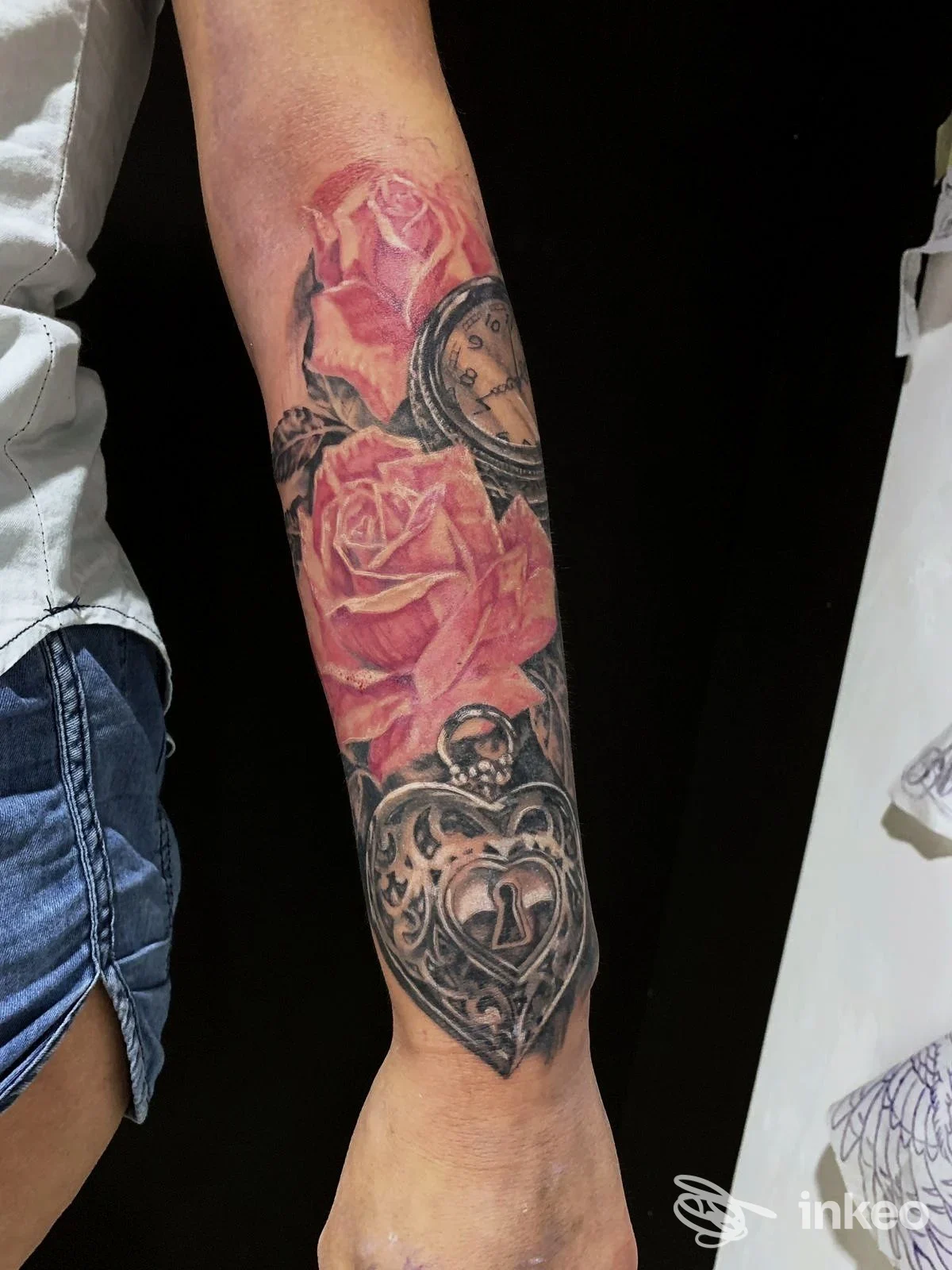 Avambraccio con tatuaggio di rose rosa e dettagli scuri, realizzato sulla pelle; non si vede volto umano.
