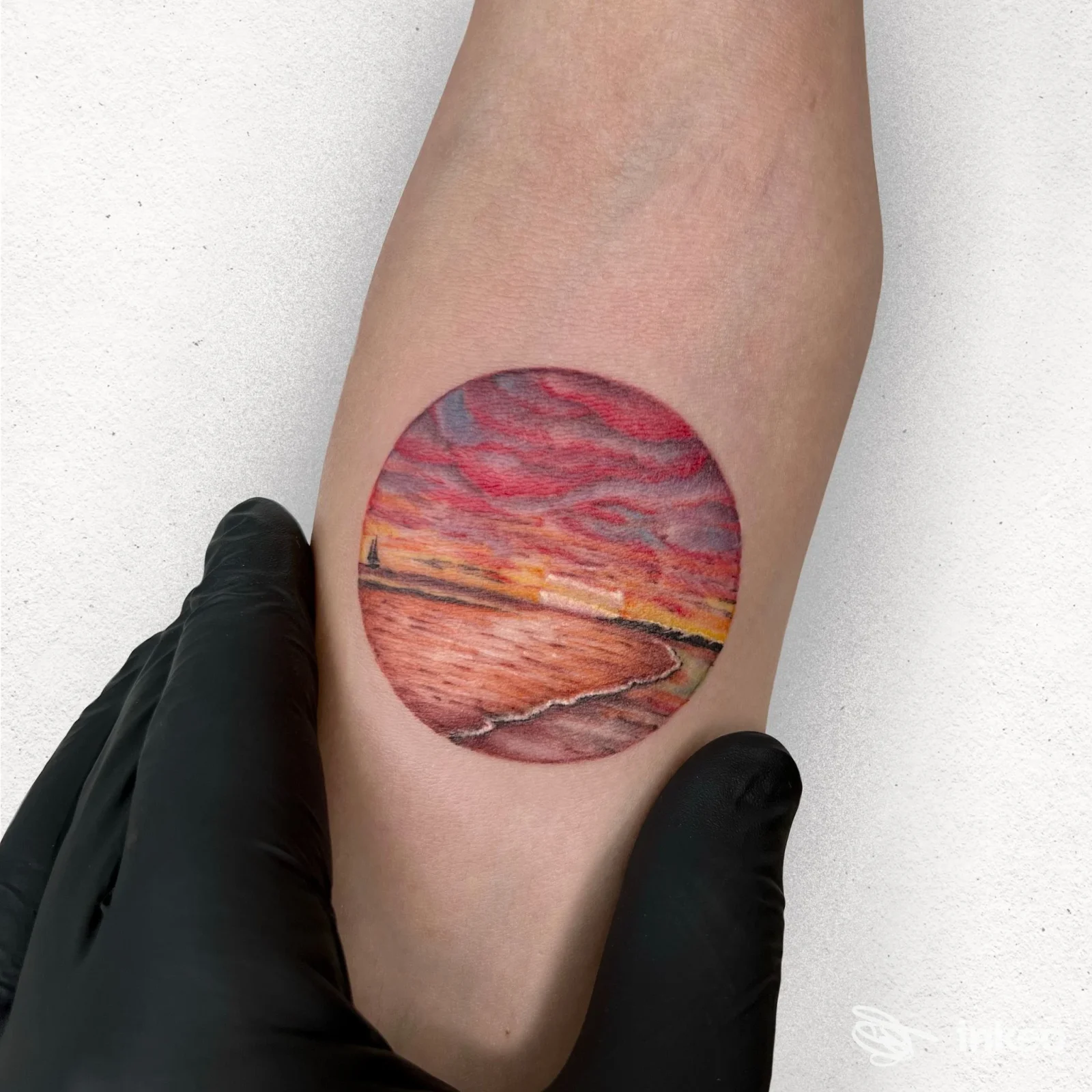 Tattoo circolare raffigurante un tramonto sulla spiaggia su pelle reale, posto sull'avambraccio, scatto preciso senza testo o watermark. Studio Urto Tattoo Shop, Cesena.
