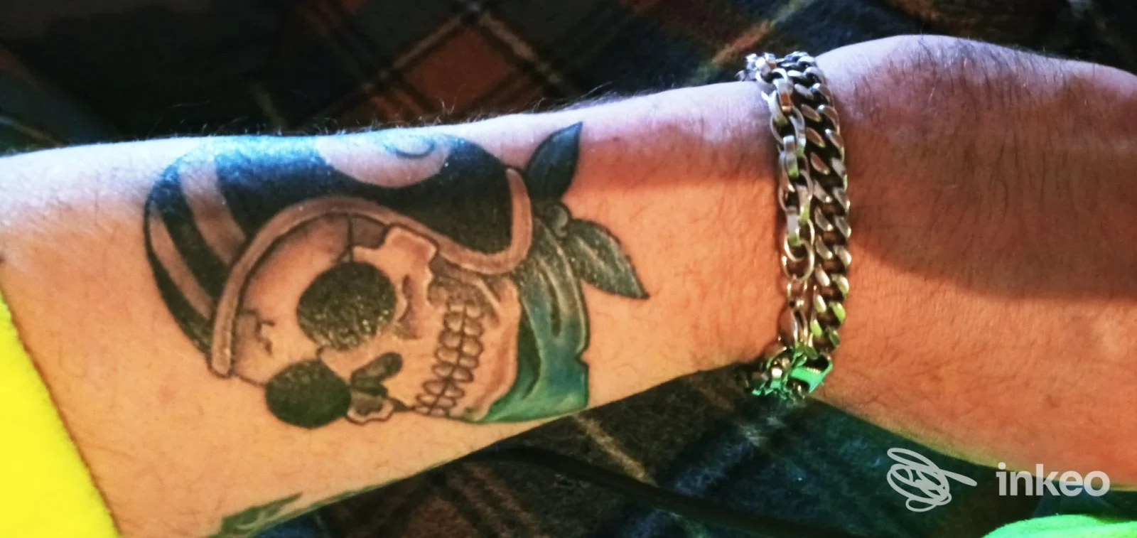 Tattoo su avambraccio sinistro: teschio con occhiali e accessori, visibile in primo piano; catena al polso, pelle non modificata. Studio Sabry Cobra Tattoo Studio, Vergato.