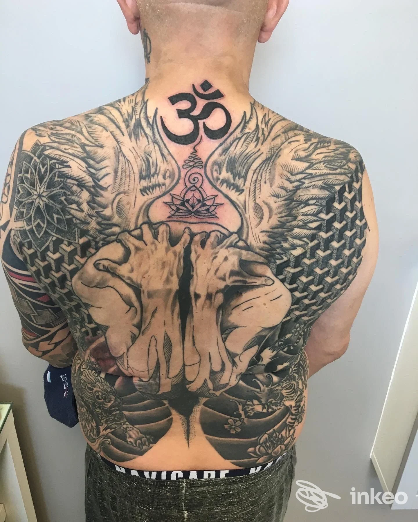 Schiena di uomo completamente tatuata, con grande simbolo Om sul collo posteriore, tatuaggio complesso che occupa tutta la schiena e le spalle, foto dall'indietro.