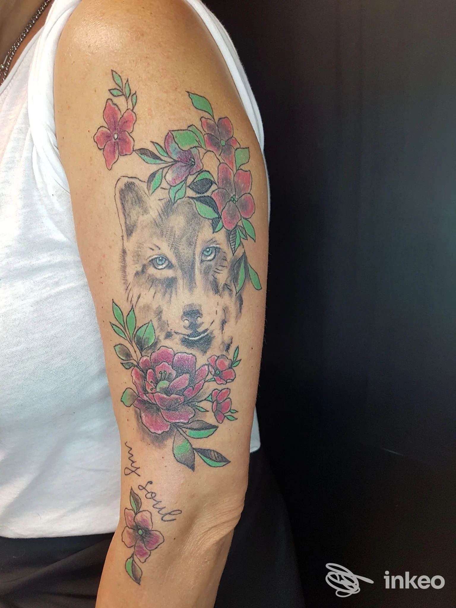 Tattoo realistico di una volpe con fiori rosa e foglie verdi sull’avambraccio, colori vividi e dettagli nitidi, sfondo scuro.