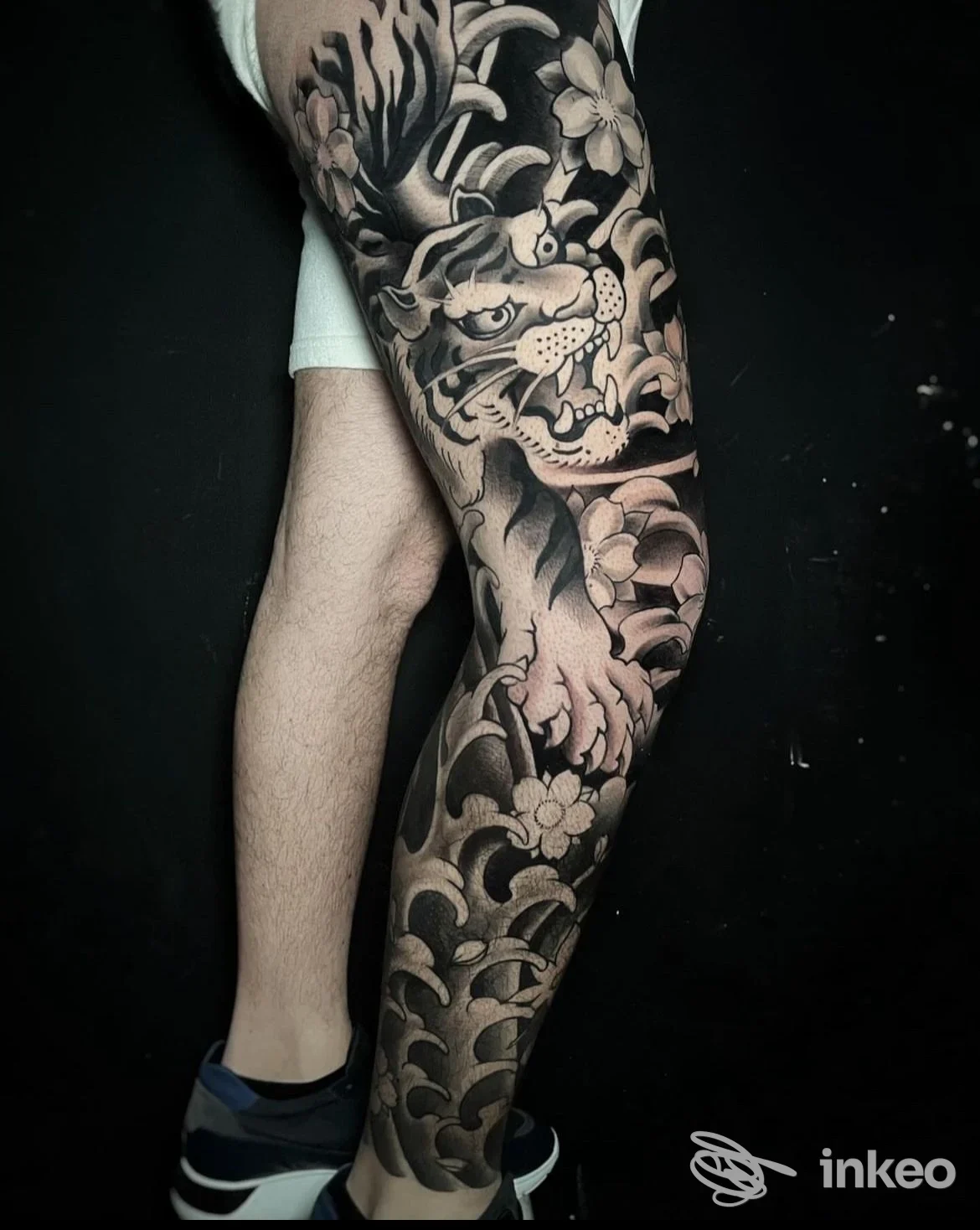 Tattoo completo della gamba destra con motivi floreali e figura animale, realizzazione su pelle visibile, sfondo scuro.
