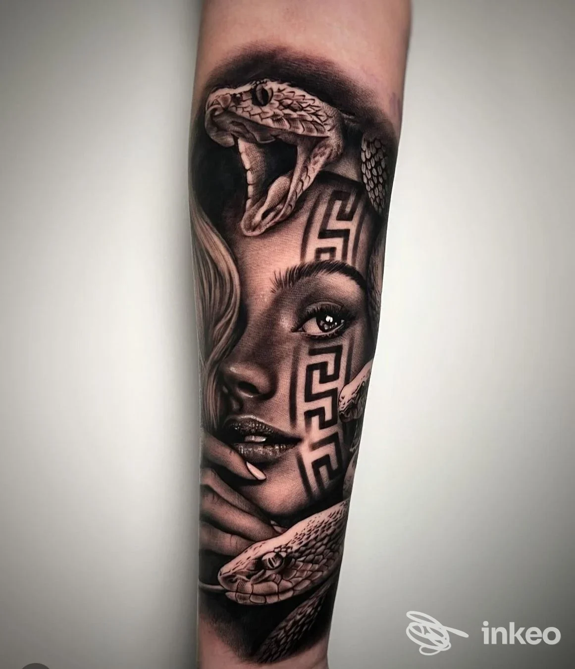 Avambraccio con un tatuaggio realistico raffigurante una testa di serpente e una donna con motivi geometrici sul volto, in tonalità nero/grigio.
