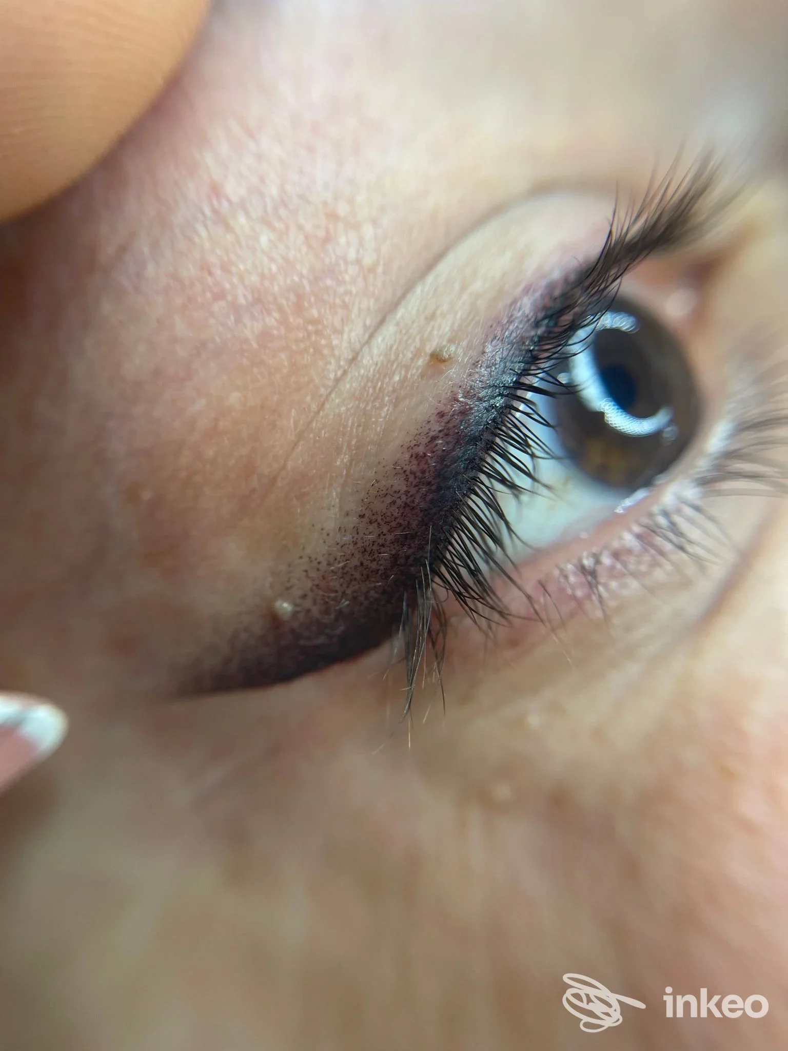 Trucco permanente perimetrale sull’occhio, visibile in primo piano, su pelle reale vicino alle ciglia, pigmento marrone scuro.