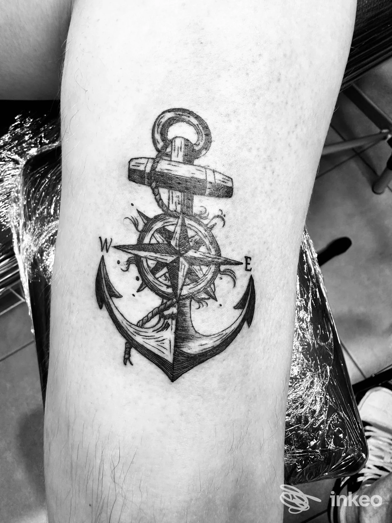 Tattoo su pelle raffigurante un'ancora con timone e rosa dei venti sull’avambraccio, scatto singolo privo di volto o testo sovrapposto.