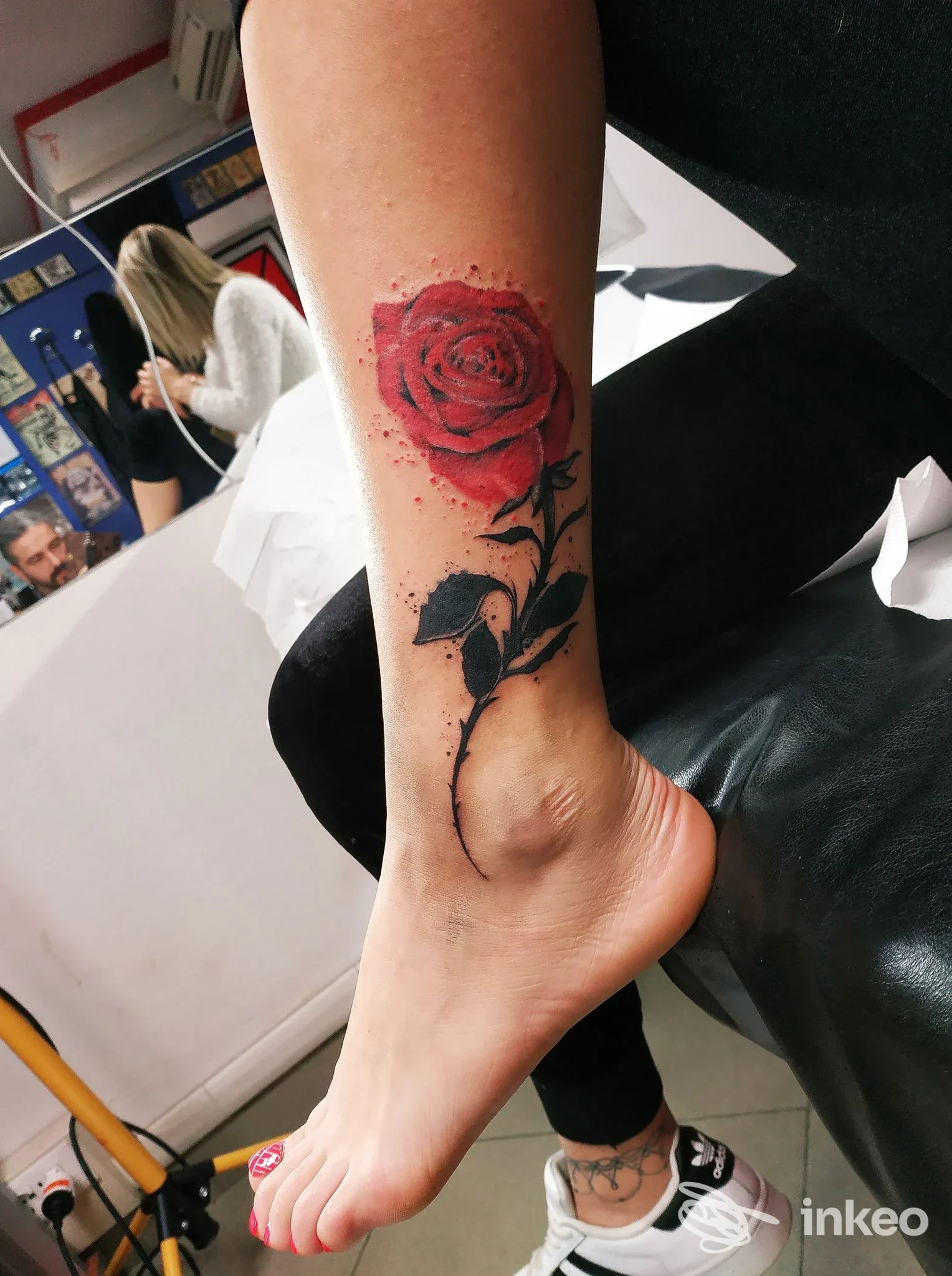 Una gamba con un tatuaggio realistico di rosa rossa sul polpaccio, visibile su una panca di studio fotografico.