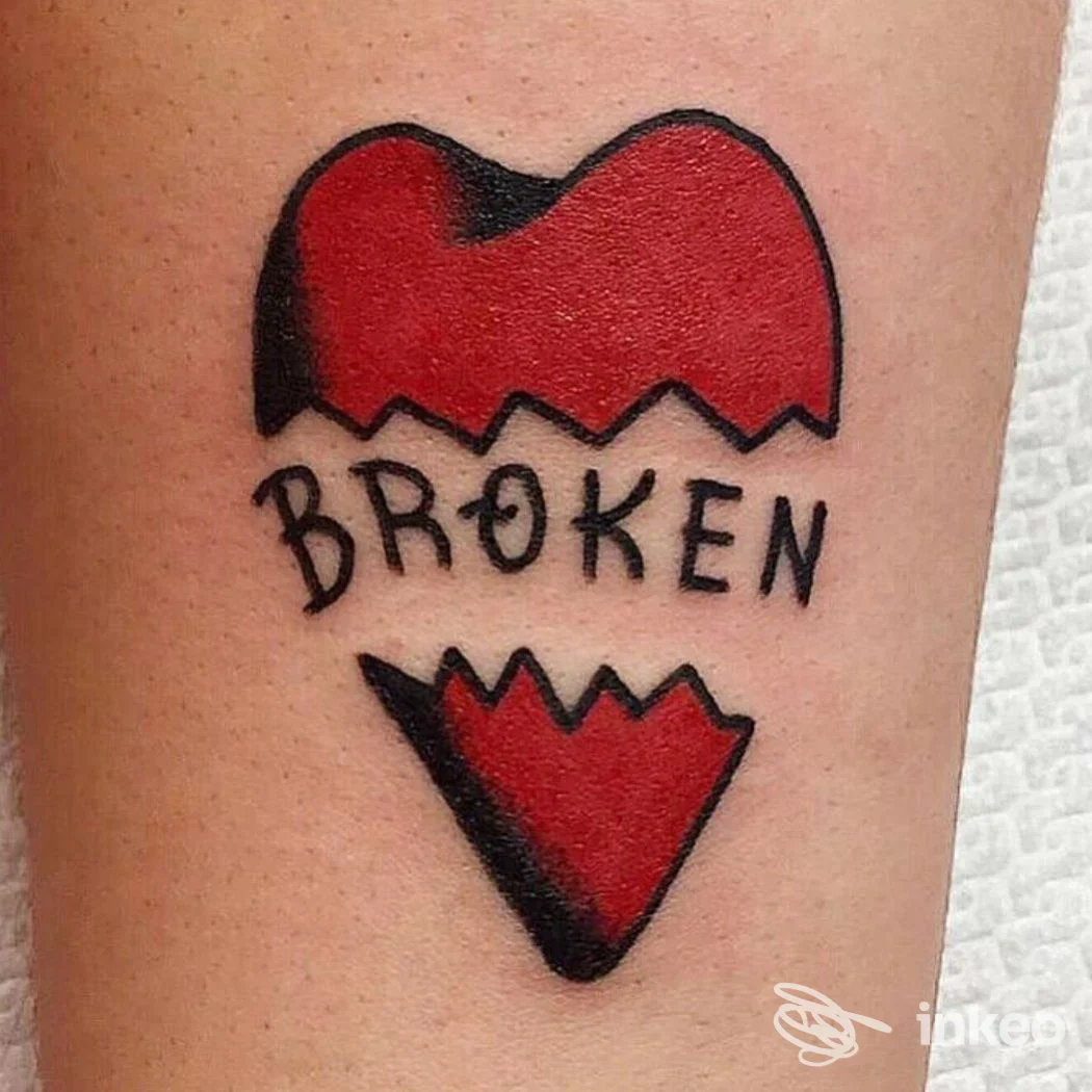 Tattoo su pelle di braccio raffigurante un cuore rosso spezzato con bordo nero e la parola BROKEN scritta in nero, foto singola.