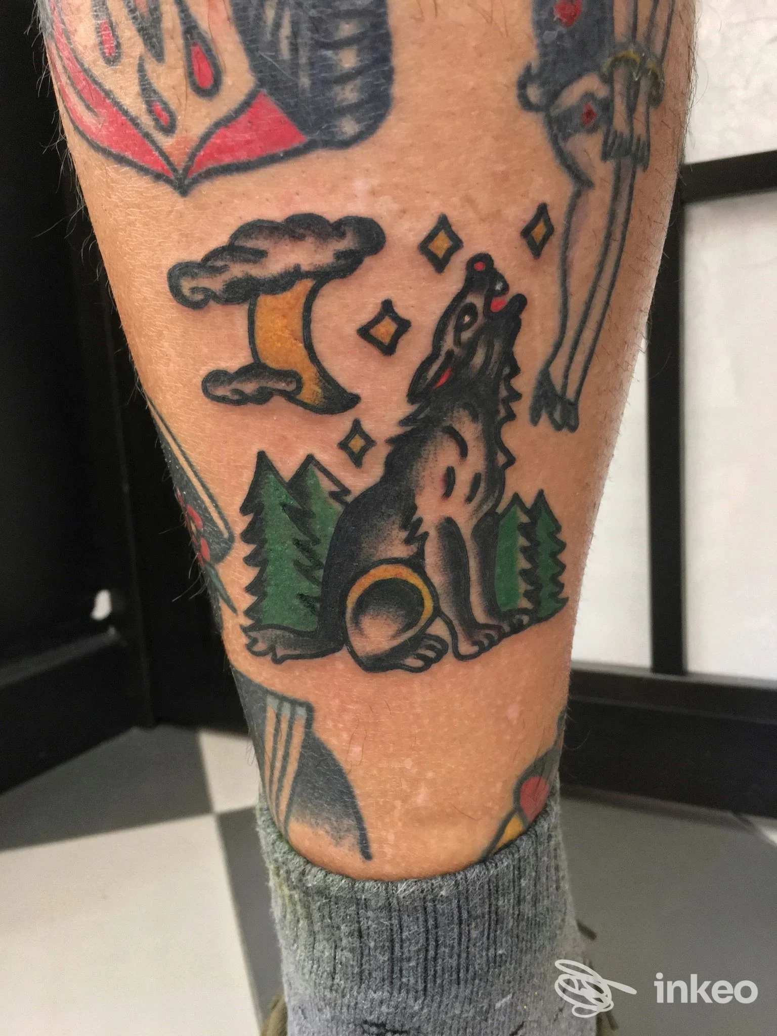 Tattoo sul polpaccio raffigurante un animale che ulula tra alberi verdi e una luna gialla, contorni neri e colori vivaci, eseguito presso Body Markings a Bologna.