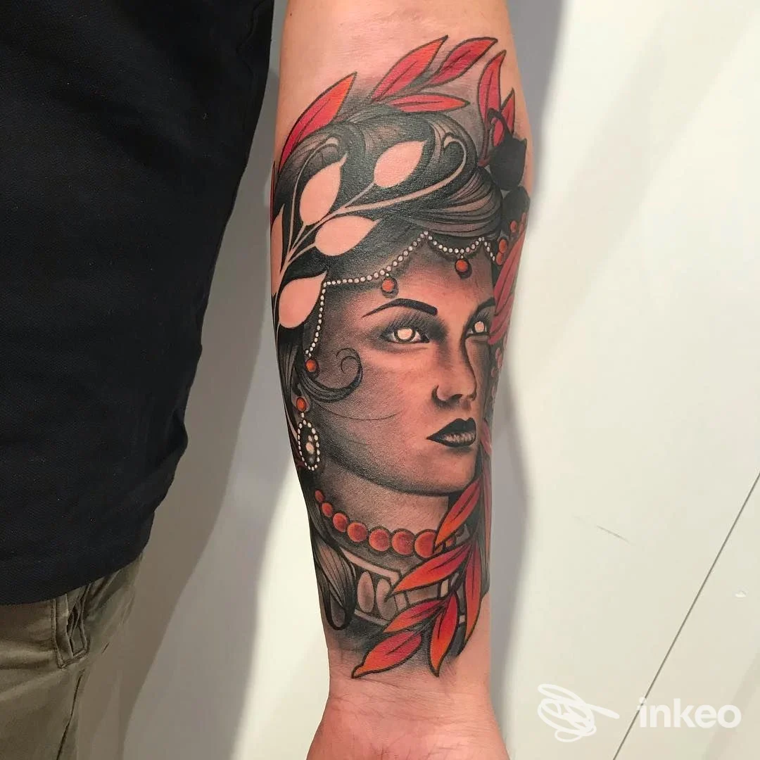 Tattoo realistico su avambraccio raffigurante una donna, ornamenti, gioielli e foglie rosse in tonalità nere e grigie, realizzazione su pelle visibile.