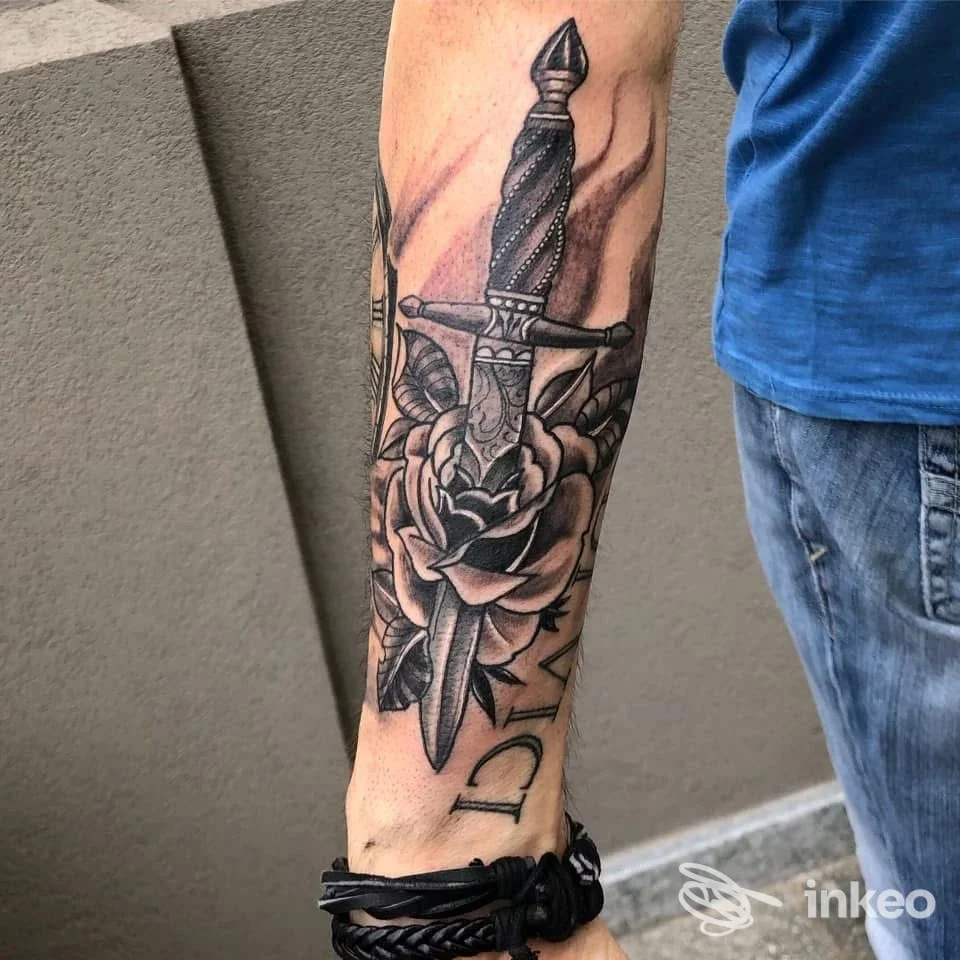 Tatuaggio a pugnale e rosa sull'avambraccio fotografato da True Love Ink a Fidenza, dettagli in bianco e nero su pelle reale.