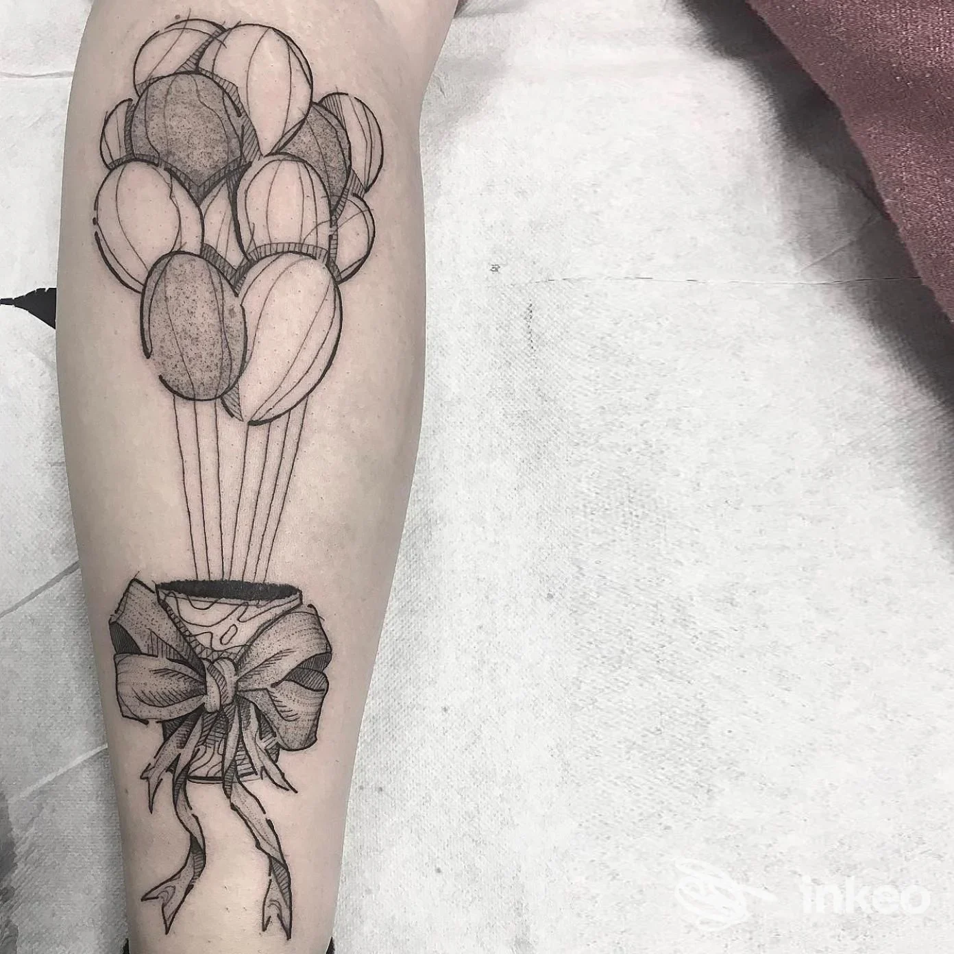 Tatuaggio su avambraccio con pacco e fiocco da cui si elevano palloncini stilizzati, fotografia del lavoro eseguito nello studio Altra Arte Tatuaggi, Faenza.