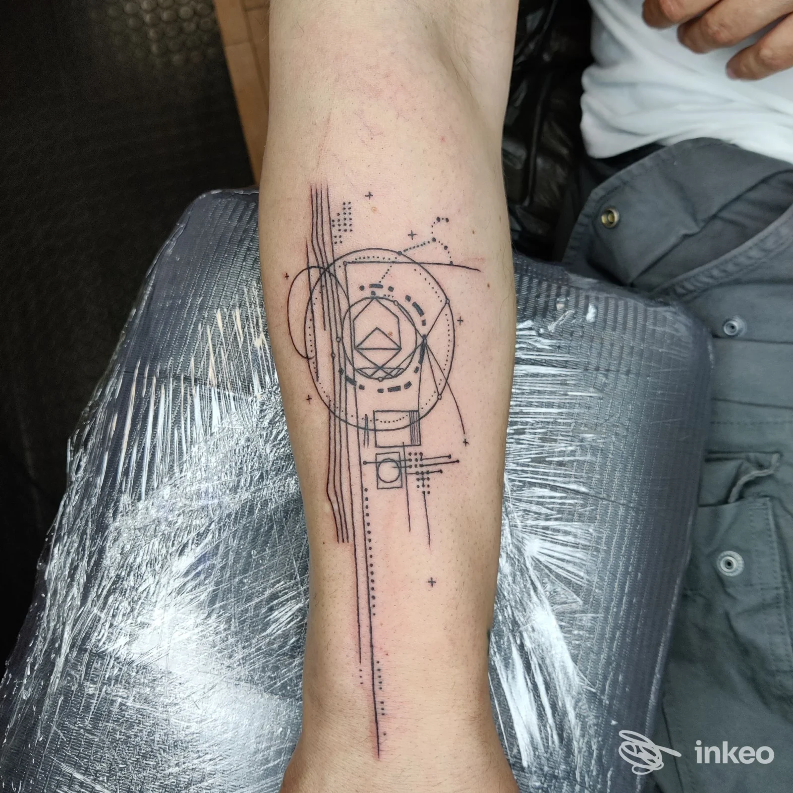 Tattoo geometrico su avambraccio: linee verticali, cerchi e piccoli motivi decorativi incisi sulla pelle, ritratto in primo piano senza volto.