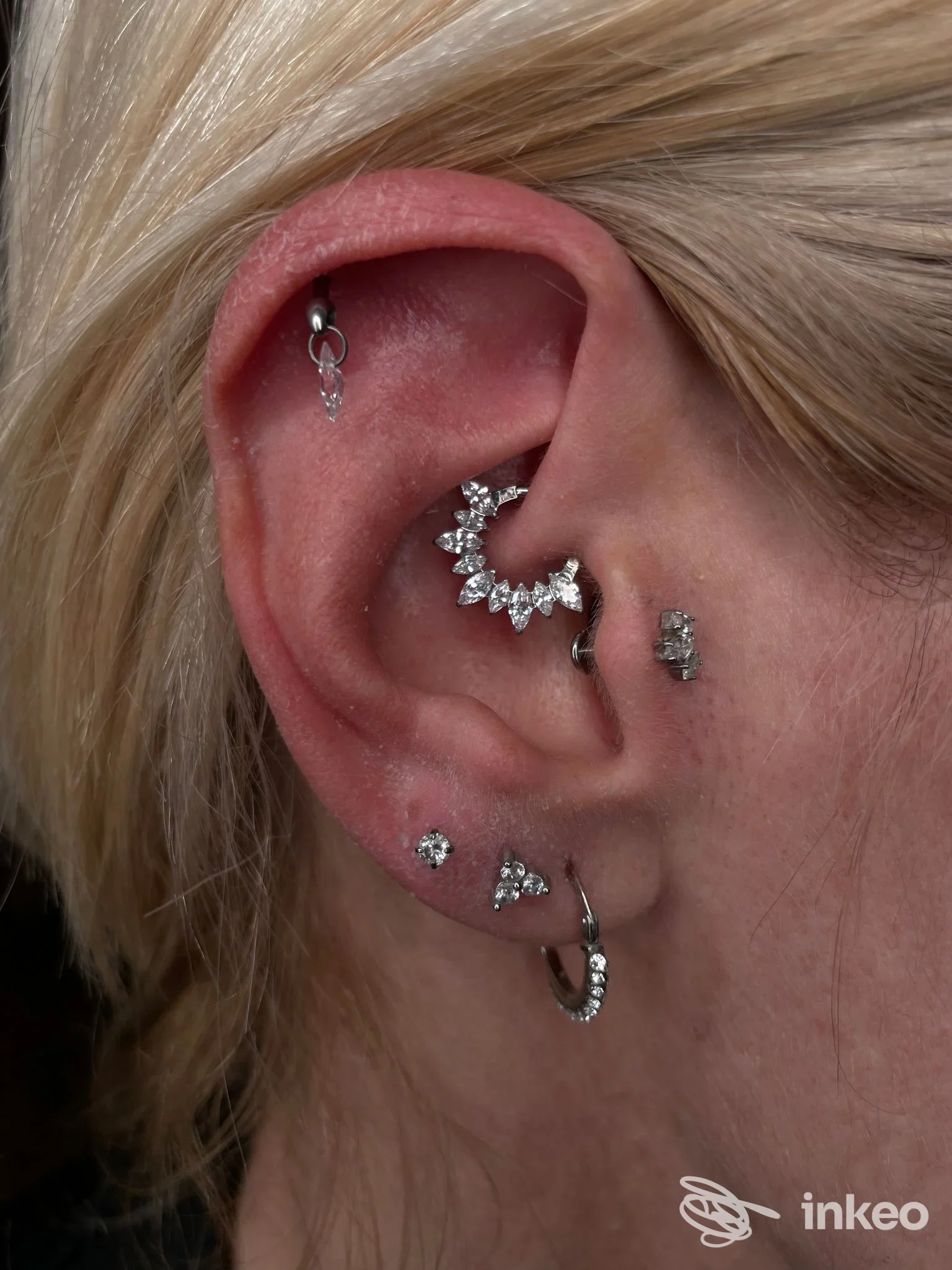 Primo piano dettagliato di un orecchio con più piercing in gioielli argentati e brillanti realizzati da AdamantioTattoo&Piercing a Piacenza.