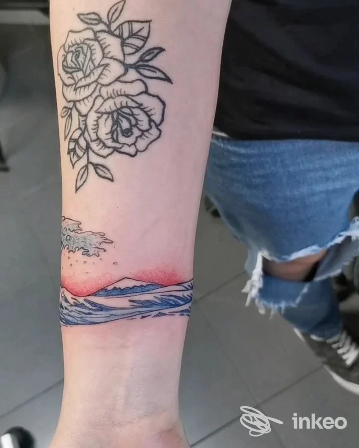 Tatuaggi su avambraccio: rose a linee nere e una fascia paesaggistica colorata al polso. God Save The Queen - Tattoo Shop, Monte San Pietro.