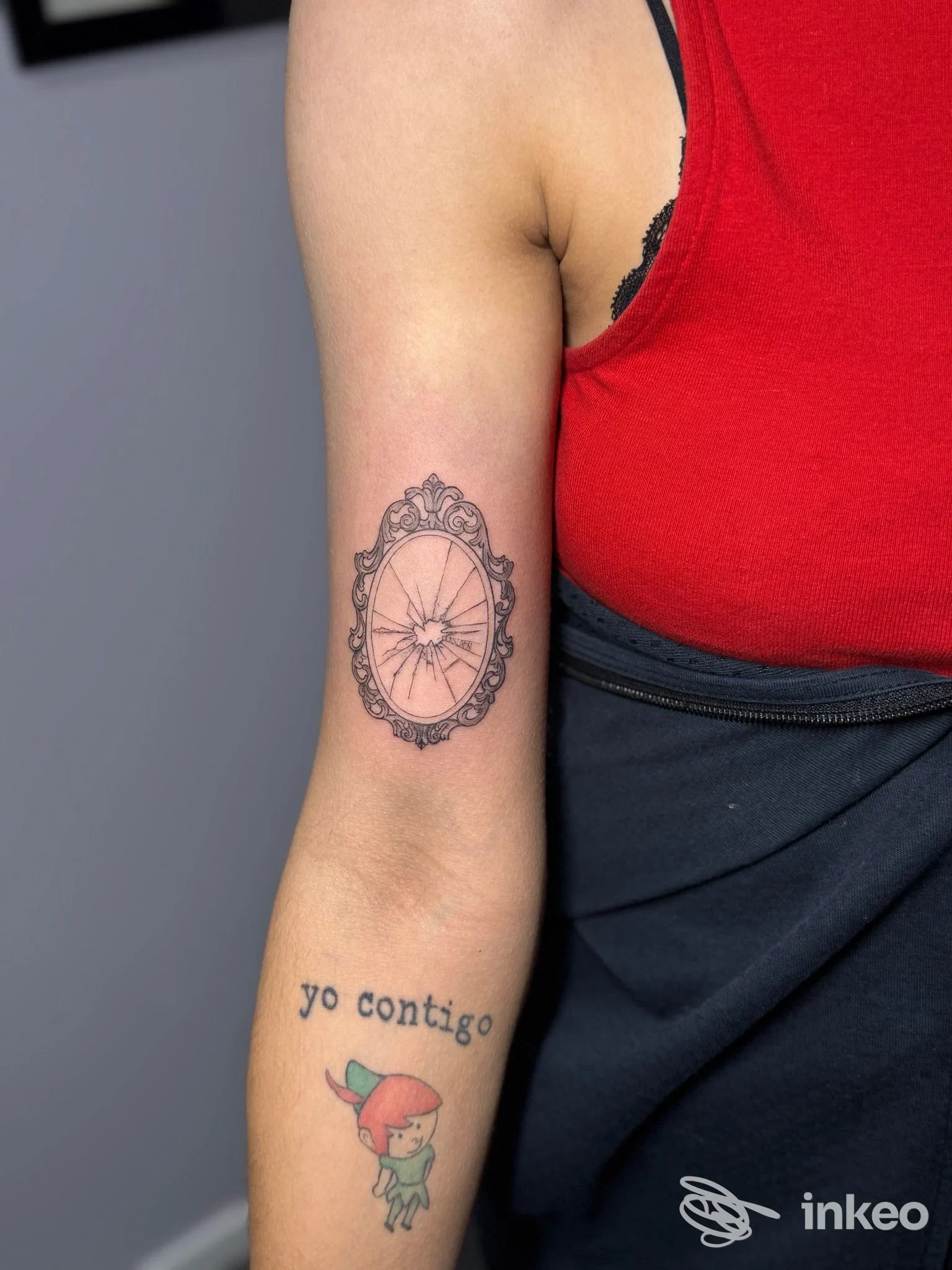 Tatuaggi sul braccio: cornice ovale ornata sul bicipite e scritta "yo contigo" con piccolo personaggio. God Save The Queen - Tattoo Shop, Monte San Pietro.