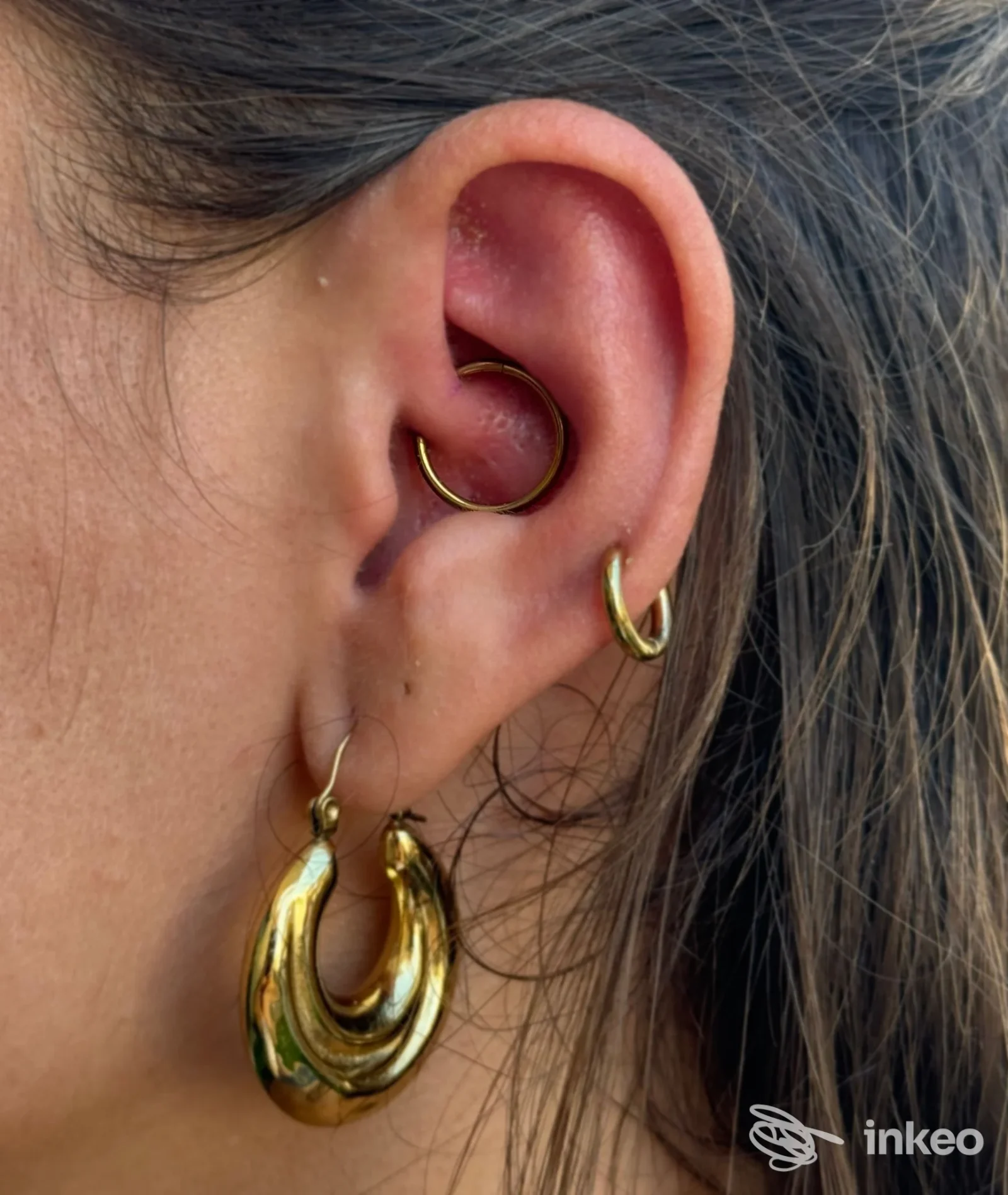 Primo piano di un orecchio con tre piercing dorati (tragus/helix e lobo). Immagine fornita da Piercer Albert, Rimini.
