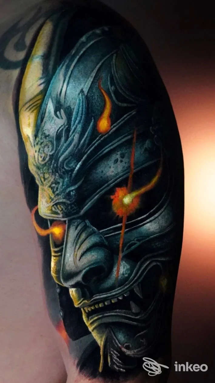 Tattoo artistico su braccio: dettaglio di un tatuaggio con una testa demoniaca in toni blu-grigi con accenti arancioni su pelle.
