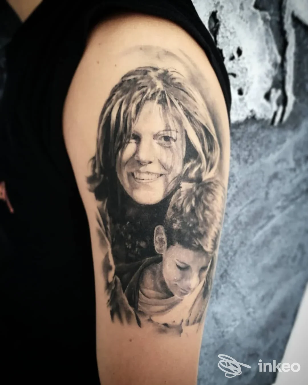 Tatuaggio realistico in bianco e nero sul braccio superiore: ritratti di una donna e di un bambino. Black Dollar Tattoo Gallery, Ramiola.