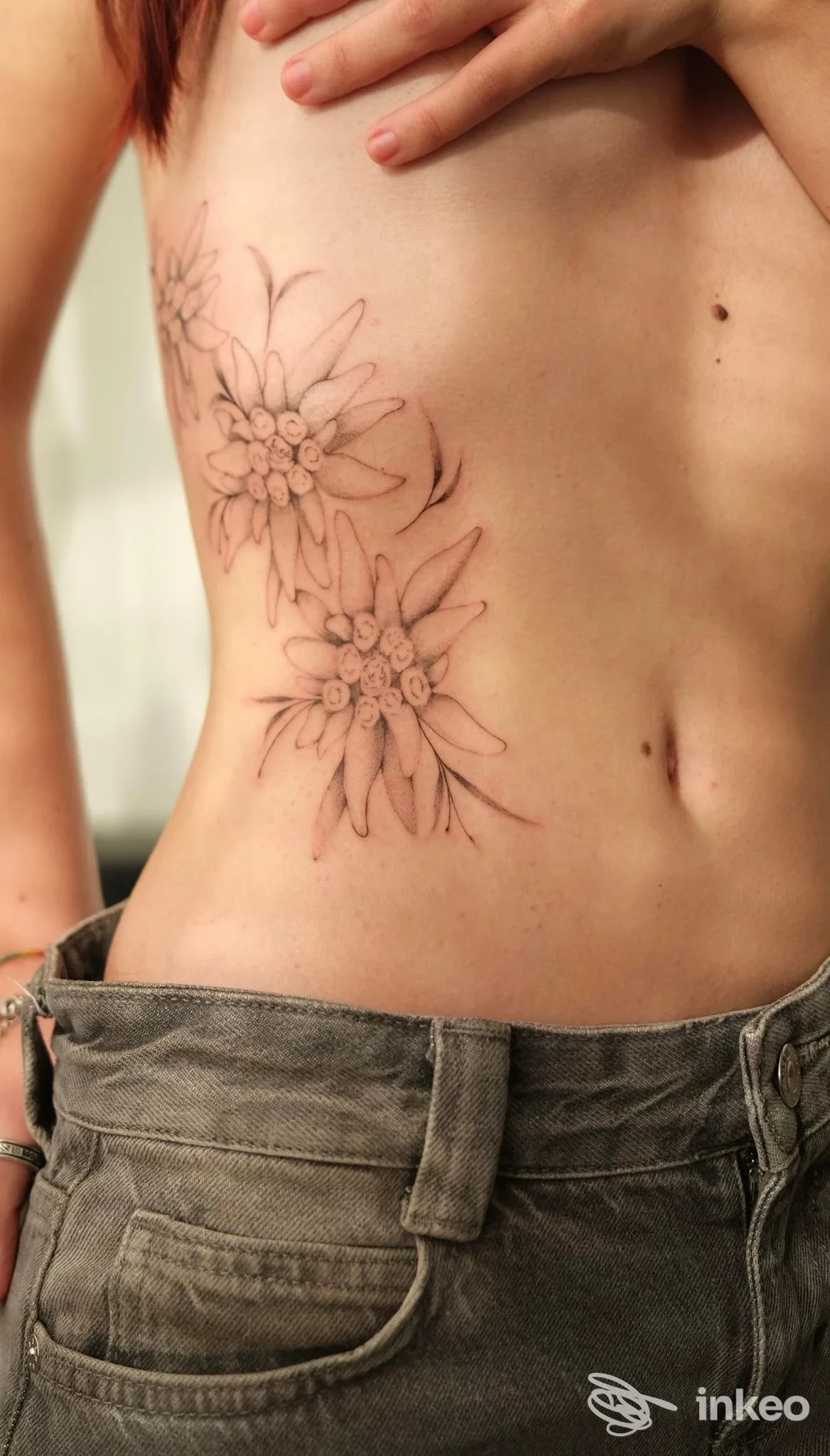 Tatuaggio a linee sottili con due fiori sul fianco di una persona, fotografia per Klinti Studio Modena.