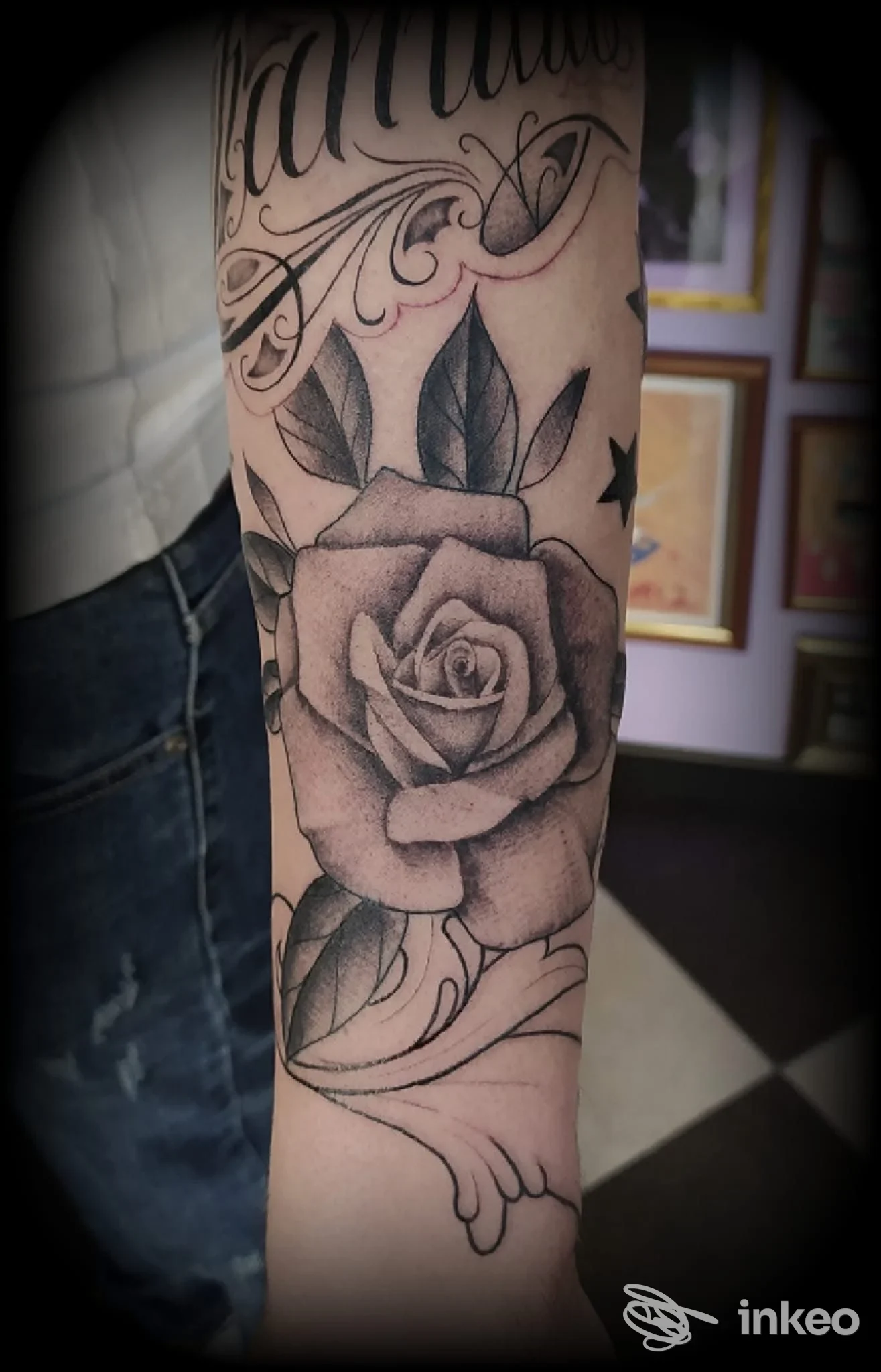 Tattoo realistico di rosa sull’avambraccio sinistro, con foglie e decorazioni; nessun volto visibile.