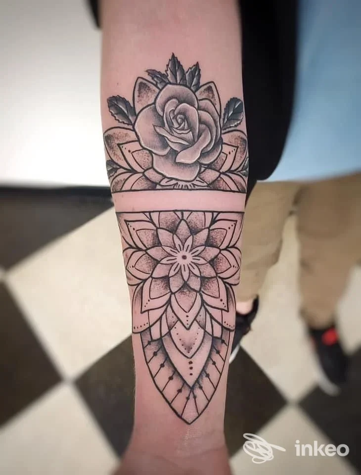 Tattoo realistico su pelle: rosa in alto e motivo mandala geometrico che scende sull’avambraccio, tonalità bianco e nero.