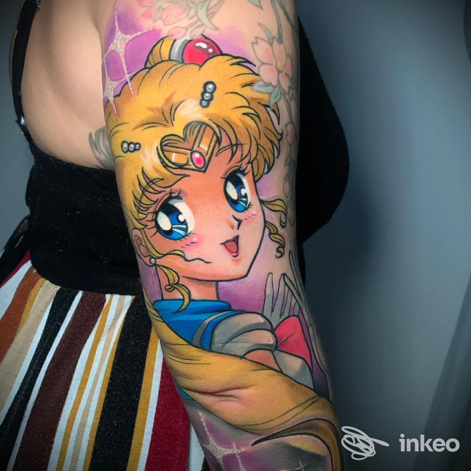 Tatuaggio a colori in stile manga su avambraccio, realizzato da SelfMade Tattoo a Lemignano, volto animato e sfondo rosa/viola.