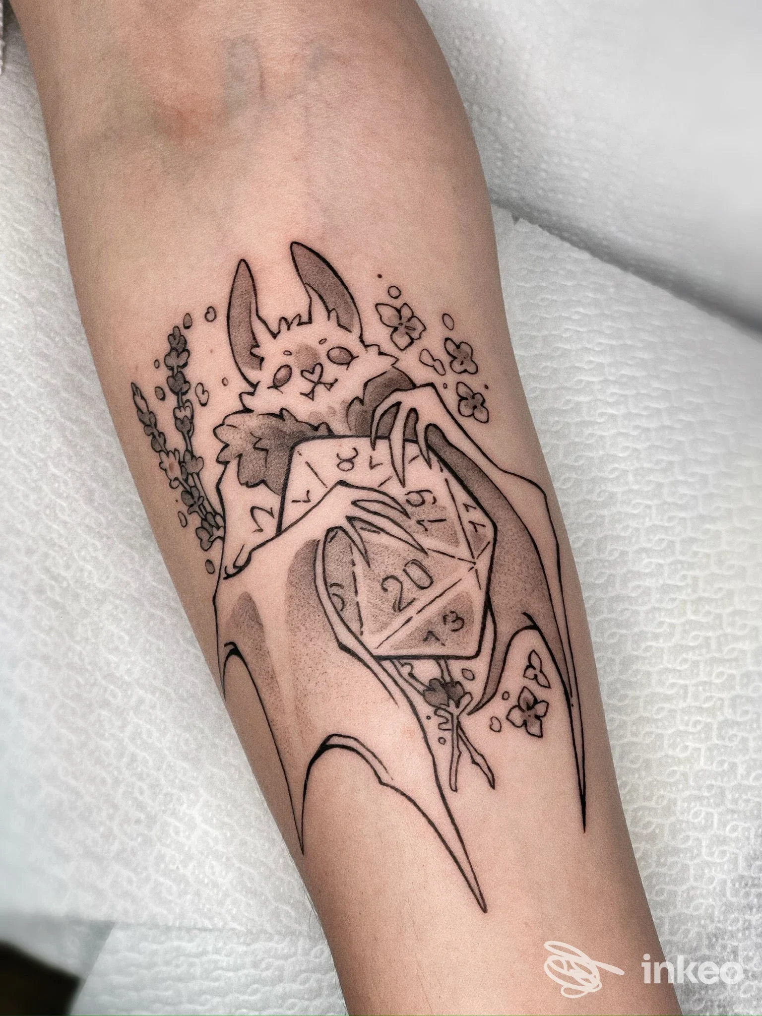Tatuaggio su avambraccio: pipistrello che tiene un dado D20, lavoro pubblicato da Bridge tattoo, Rimini.