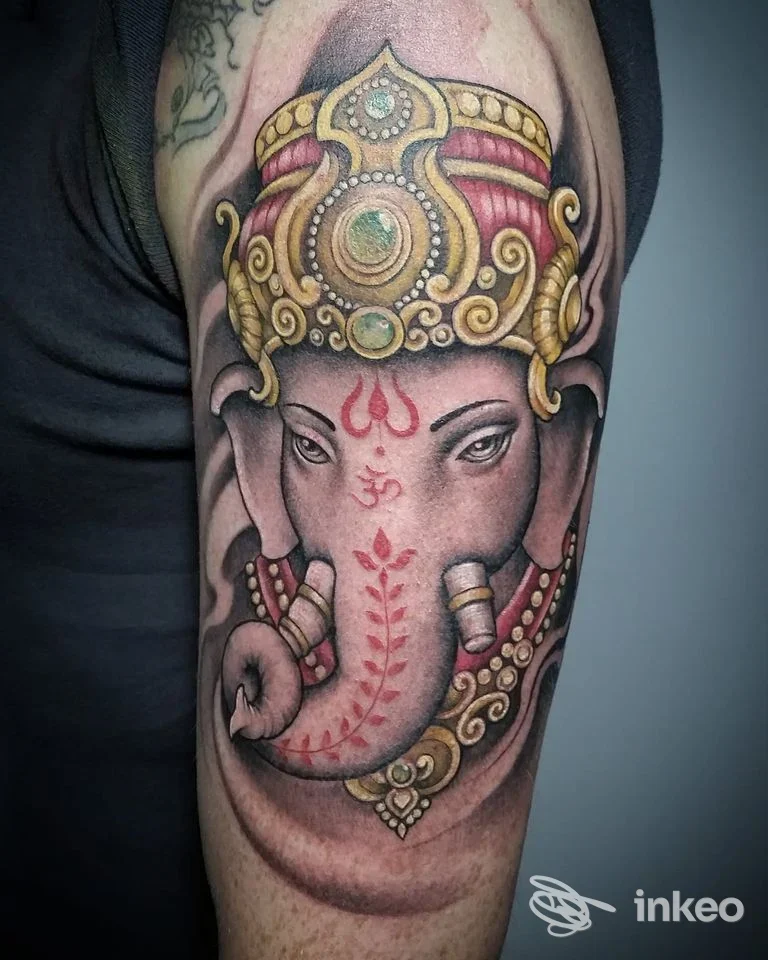 Tatuaggio raffigurante Ganesh con corona dorata e dettagli rossi sul braccio superiore, Tattoo Space Studio, Meldola.