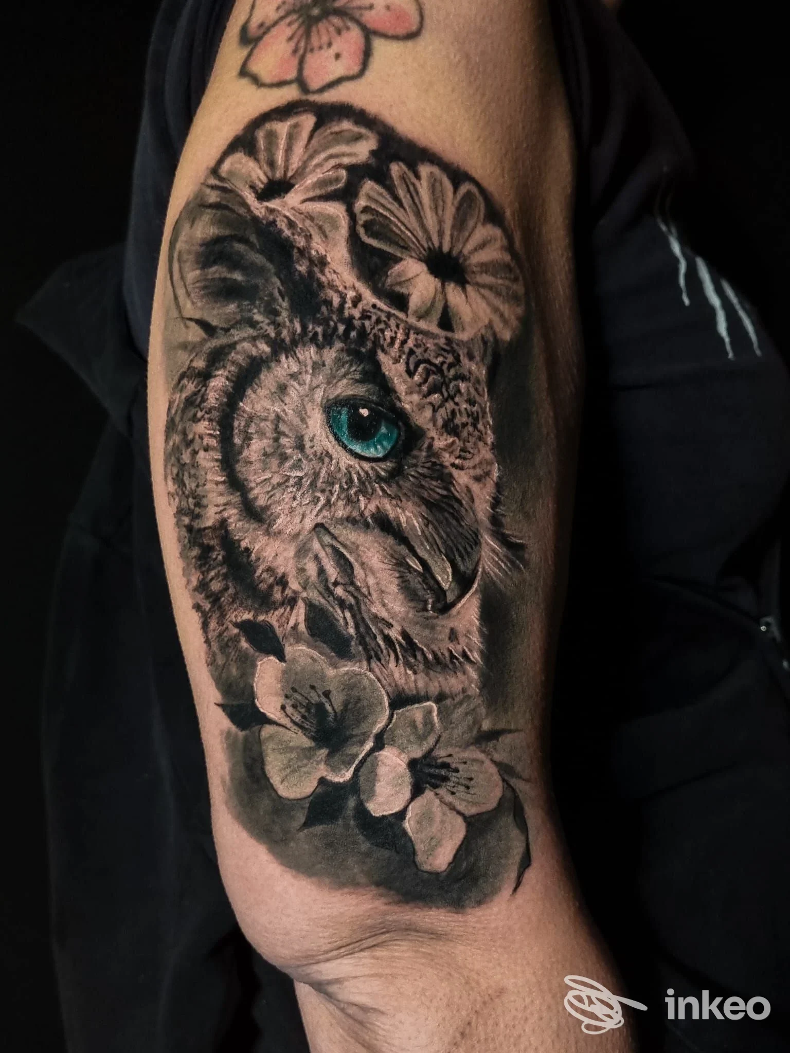 Tatuaggio realistico di civetta con occhio azzurro e fiori sull'avambraccio, Tattooificio Piacenza.