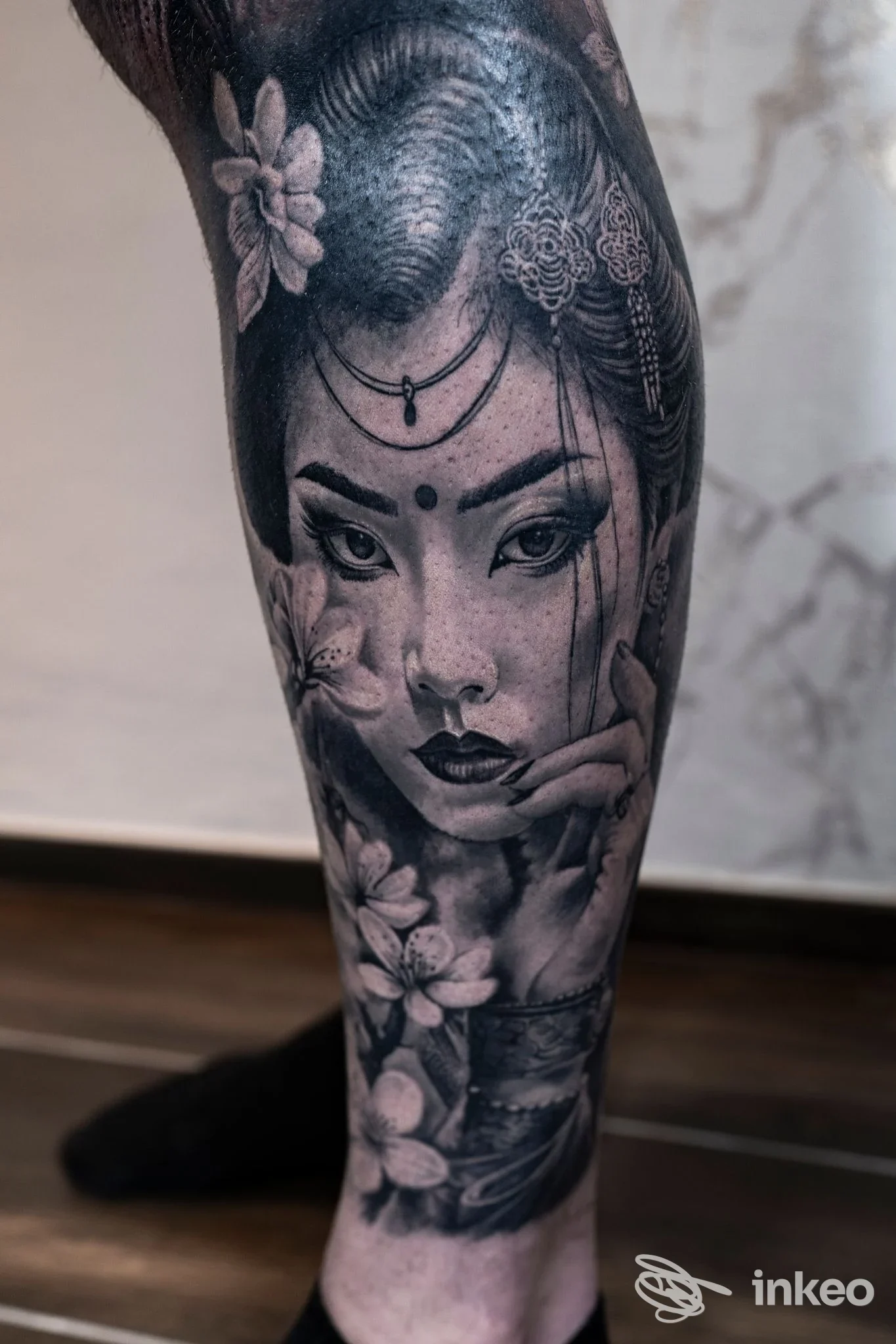 Tatuaggio realistico in bianco e nero su polpaccio con volto femminile e fiori — Riva Ink Tattoo, Rimini.