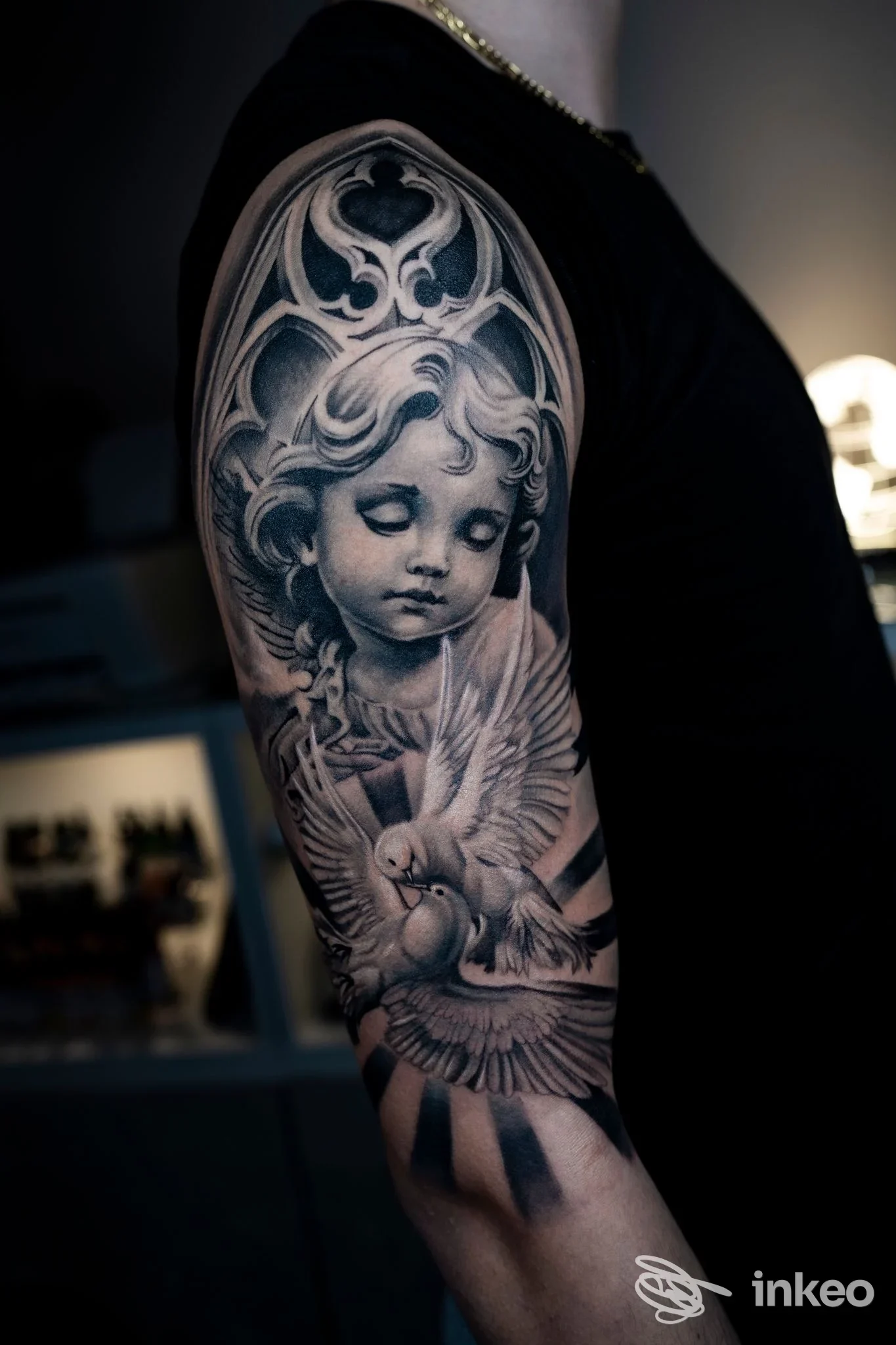 Tatuaggio black-and-grey di un angelo con colombe sul braccio superiore, lavoro di Riva Ink Tattoo e Piercing, Rimini.