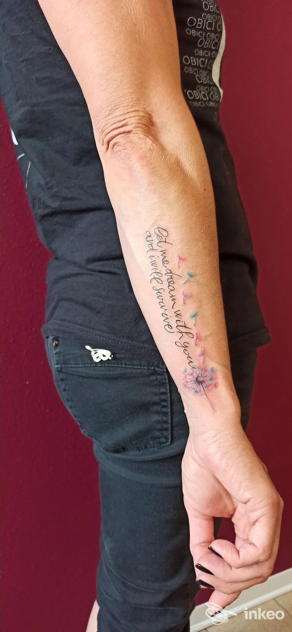 Tatuaggio testuale con piccoli fiori acquerellati sull'avambraccio sinistro, foto inviata da Ink Fede a Medolla.
