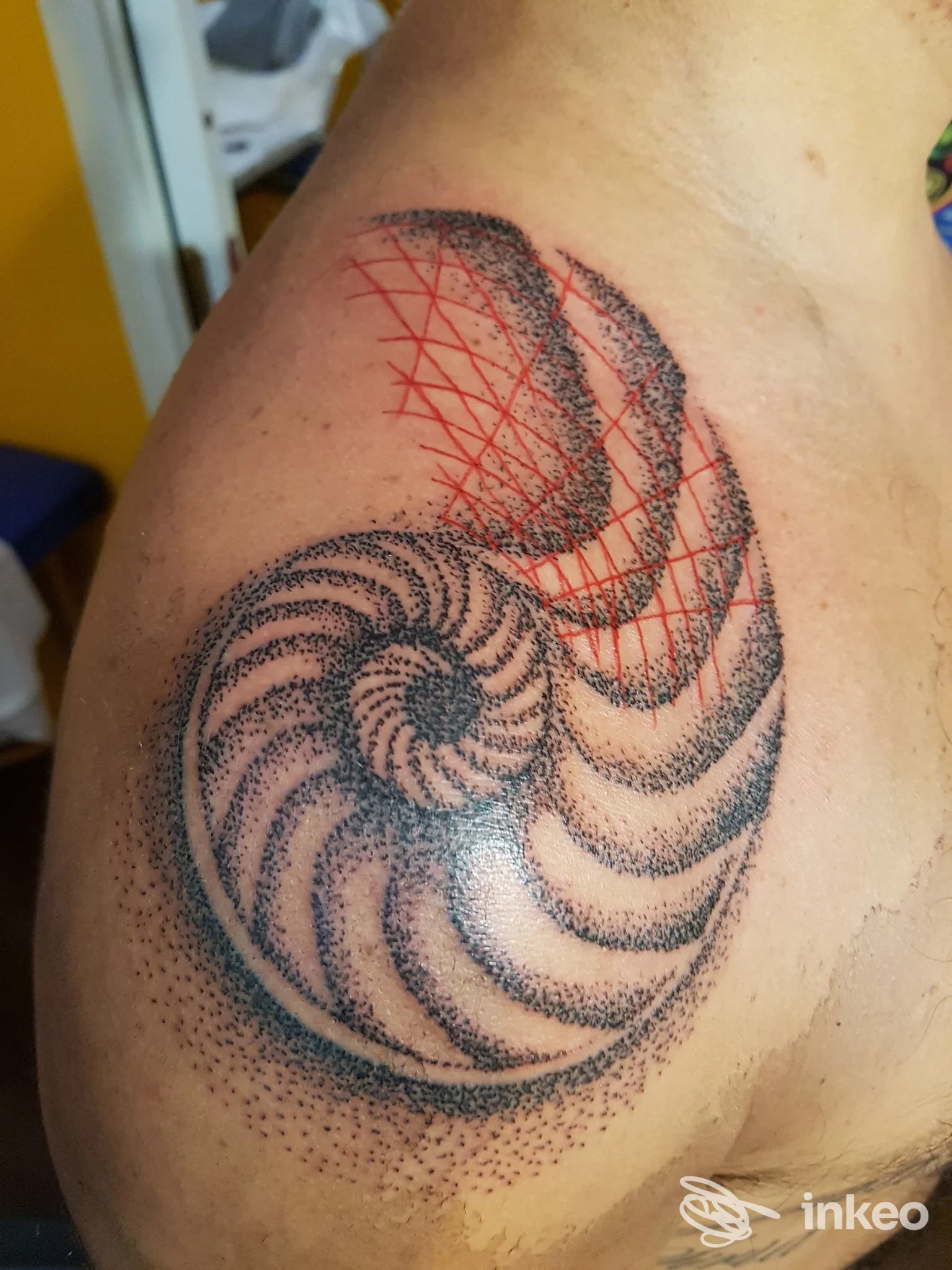 Tatuaggio a spirale in dotwork con elementi geometrici rossi sulla spalla, scatto dallo studio Max Tattoo a Casalecchio di Reno.