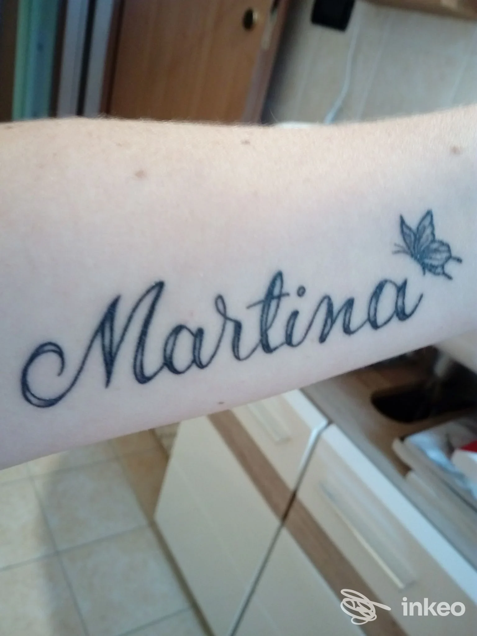 Primo piano di un tatuaggio sull'avambraccio con la scritta 'Martina' e una piccola farfalla, eseguito presso Inky Tattoo & Piercing a Bellaria-Igea Marina.