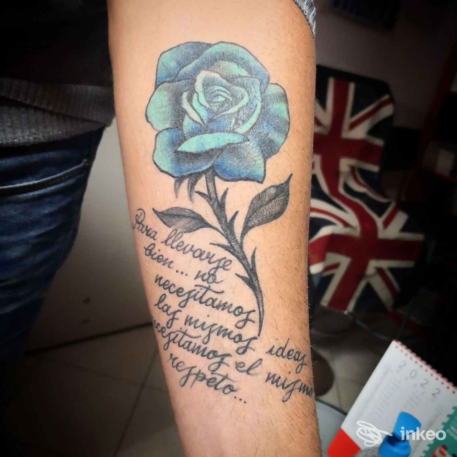 Tatuaggio di una rosa blu con foglie e testo corsivo sull'avambraccio, Venerdì 13 Tattoo Studio, Riccione.