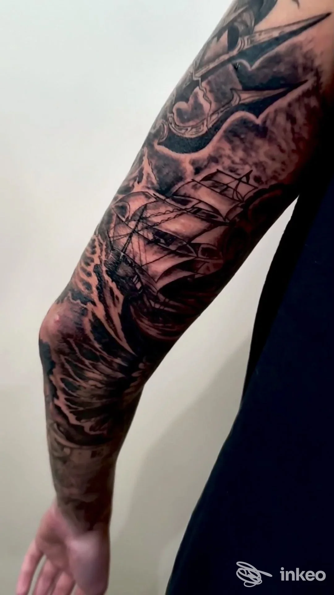 Tatuaggio realistico su braccio raffigurante una vela tra onde, realizzato direttamente sulla pelle, visibile senza volti o elementi di interfaccia; scatto singolo.