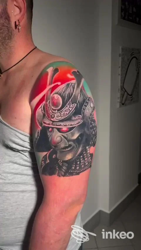 Tattoo realistico sul braccio di un uomo, stile giapponese, con maschera nera e dettagli.