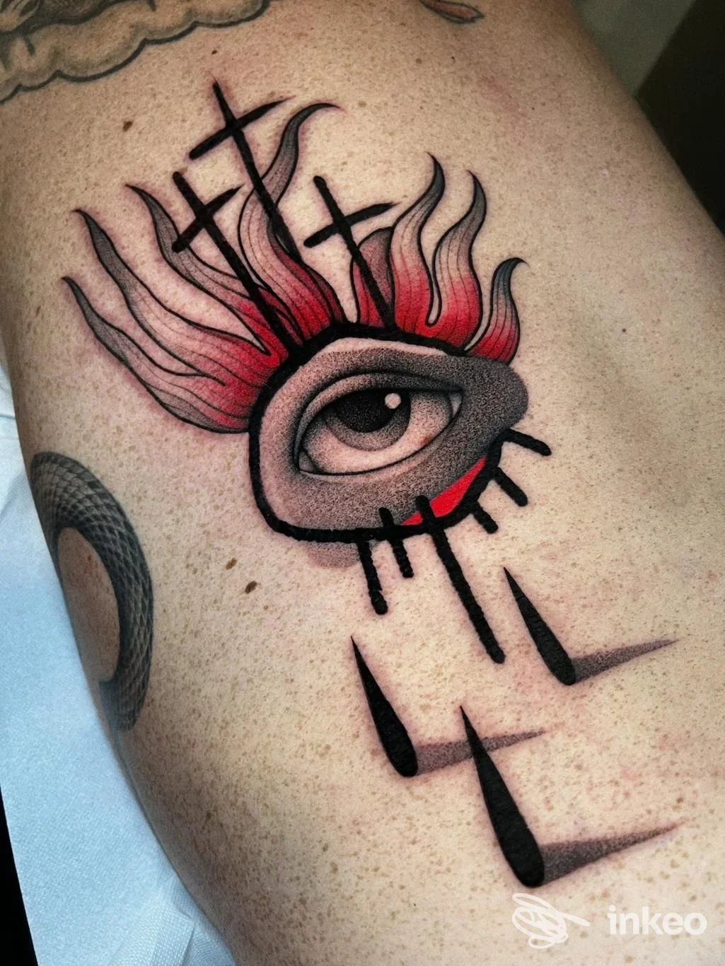 Tatuaggio con occhio stilizzato e fiamme rosse su pelle, immagine fornita da Black Gold Tattoo, Parma.