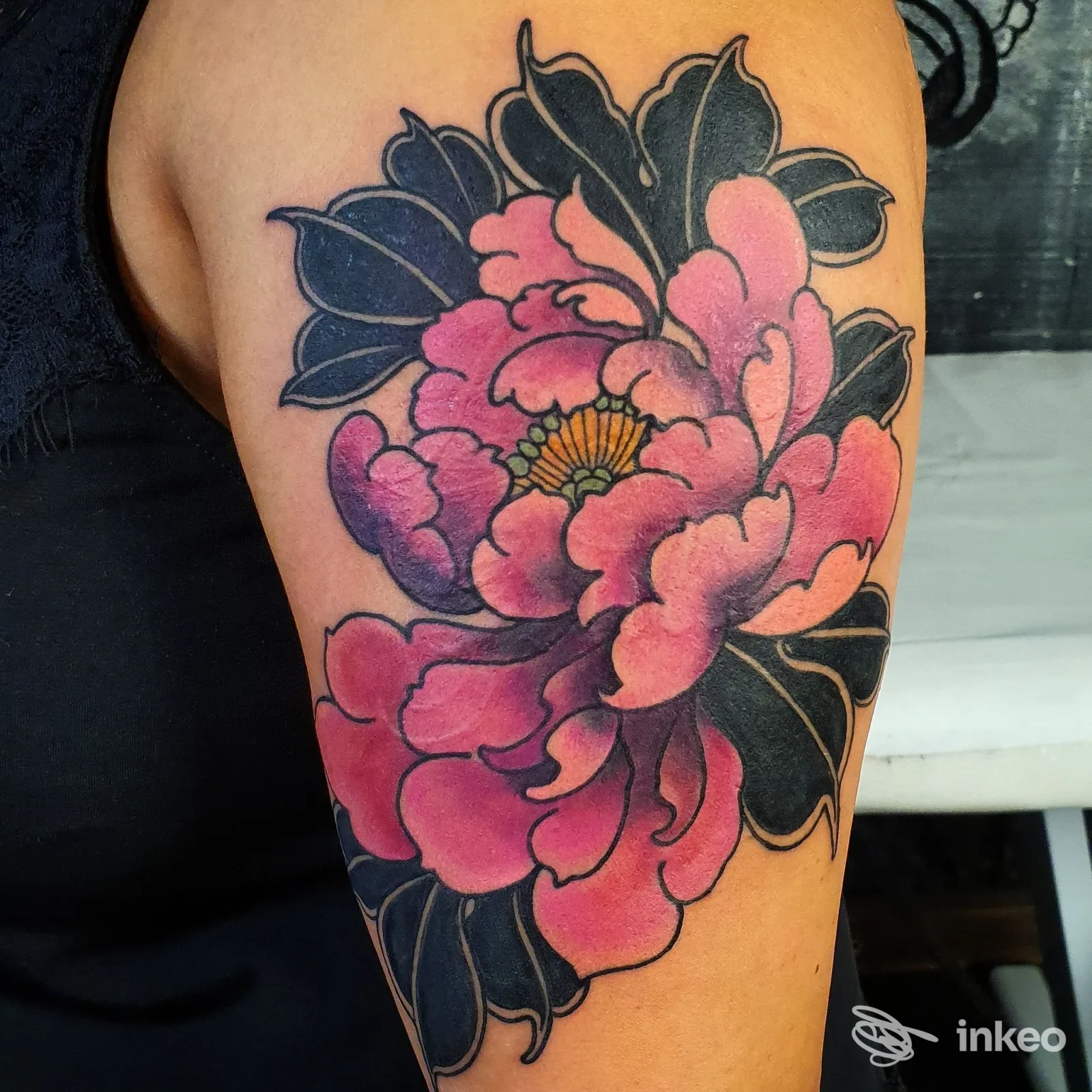 Grande fiore colorato tatuato sul braccio superiore, petali rosa e foglie nere, lavoro eseguito da Liquid EyE Tattoo Shop a Forlì.