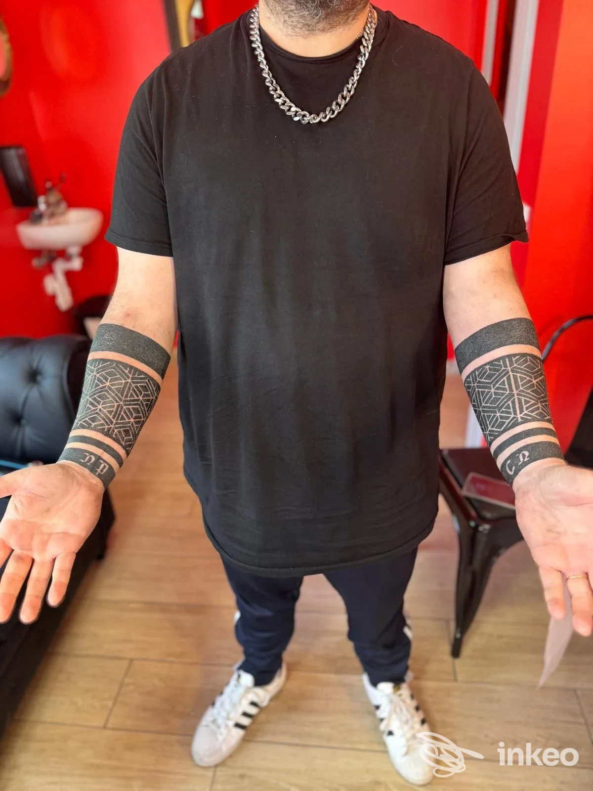 Due avambracci tatuati con fasce geometriche in uno studio (Tatta Modena Ink, Modena), persona in piedi ripresa dal petto in giù.