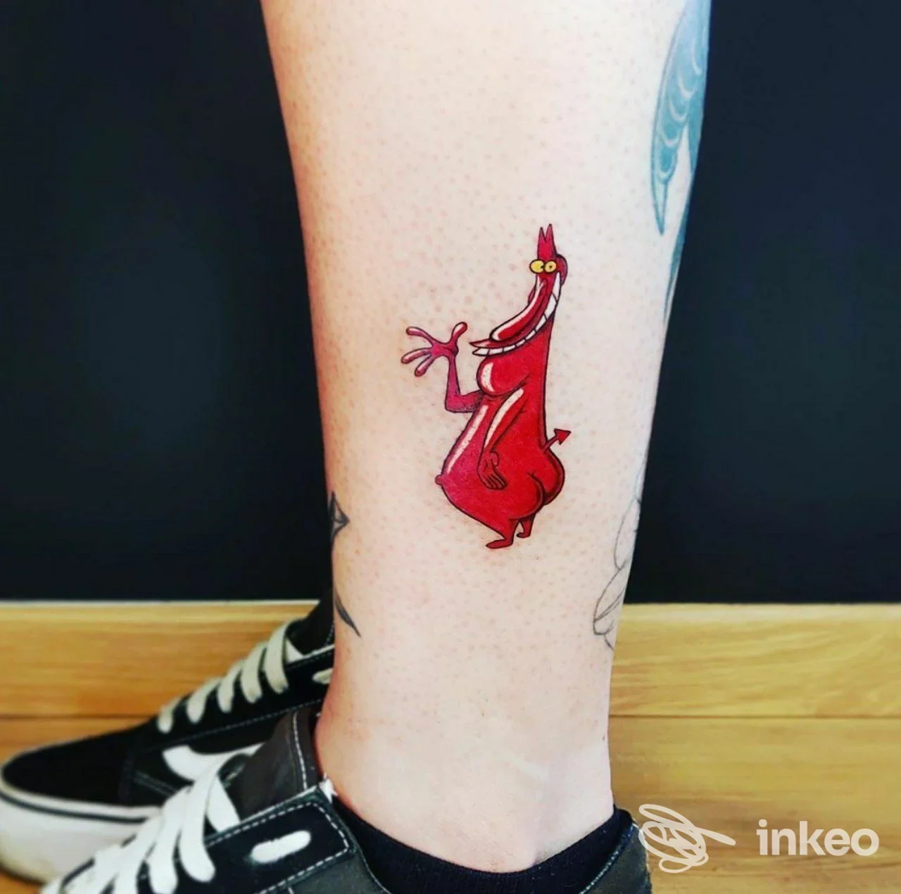 Tatuaggio colorato a tema cartoon su polpaccio, dettaglio nitido fotografato nello studio T.Beautyink a Modena, sfondo scuro e pavimento in legno.