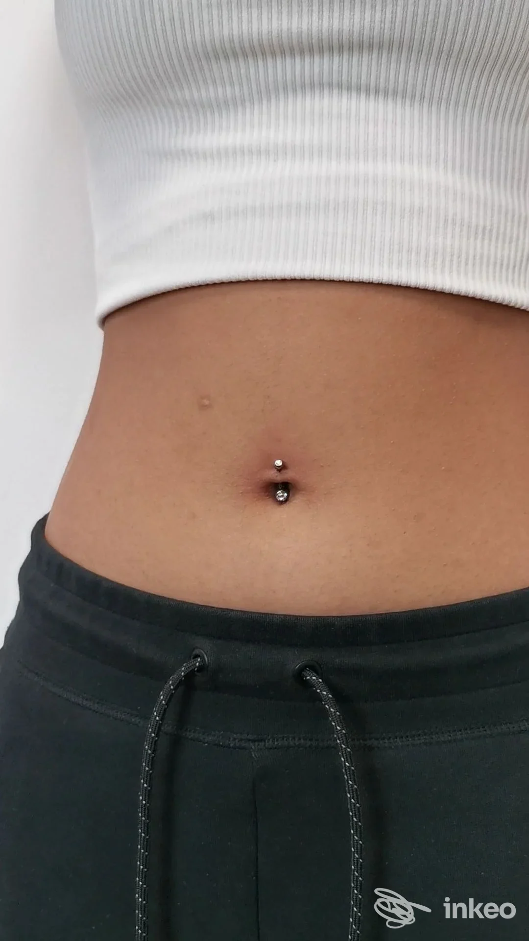 Primo piano dell'addome con piercing all'ombelico: pallina superiore e gioiello inferiore visibili su pelle naturale, foto inviata da T.Beautyink, Modena.