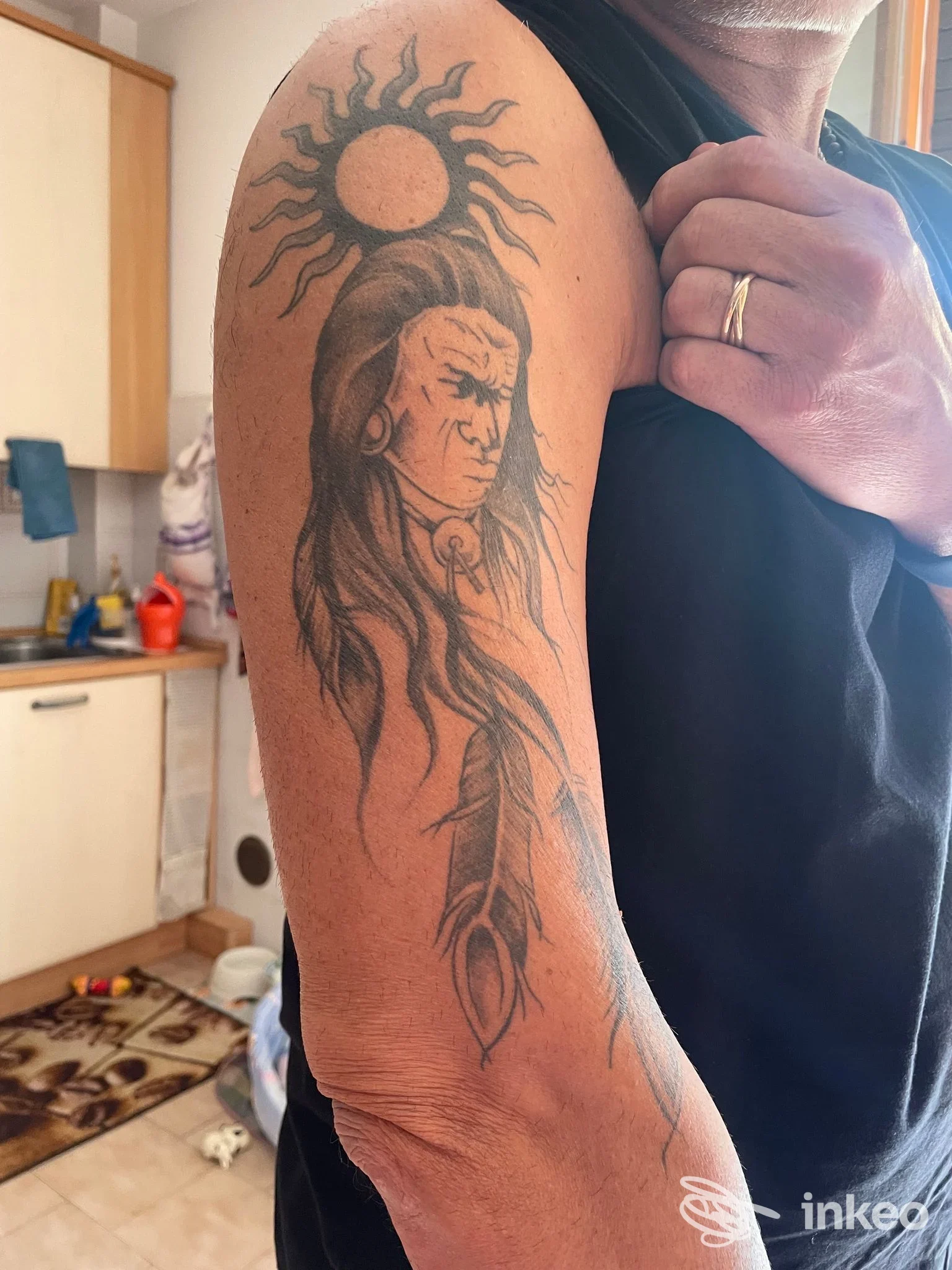 Tatuaggio su braccio superiore con volto stilizzato, piuma e sole, fotografia fornita da Lady Bulbo Lab, Calerno.