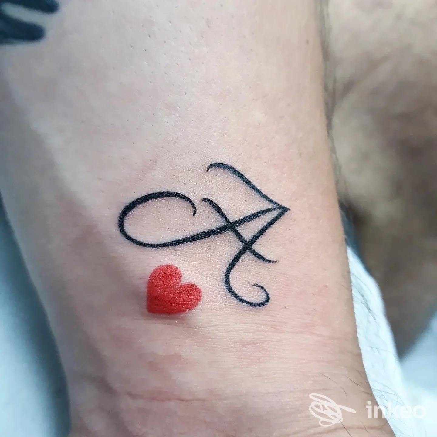 Tatuaggio con lettera A in nero e piccolo cuore rosso sull'avambraccio, realizzato da Art Design Ink, Cervia.
