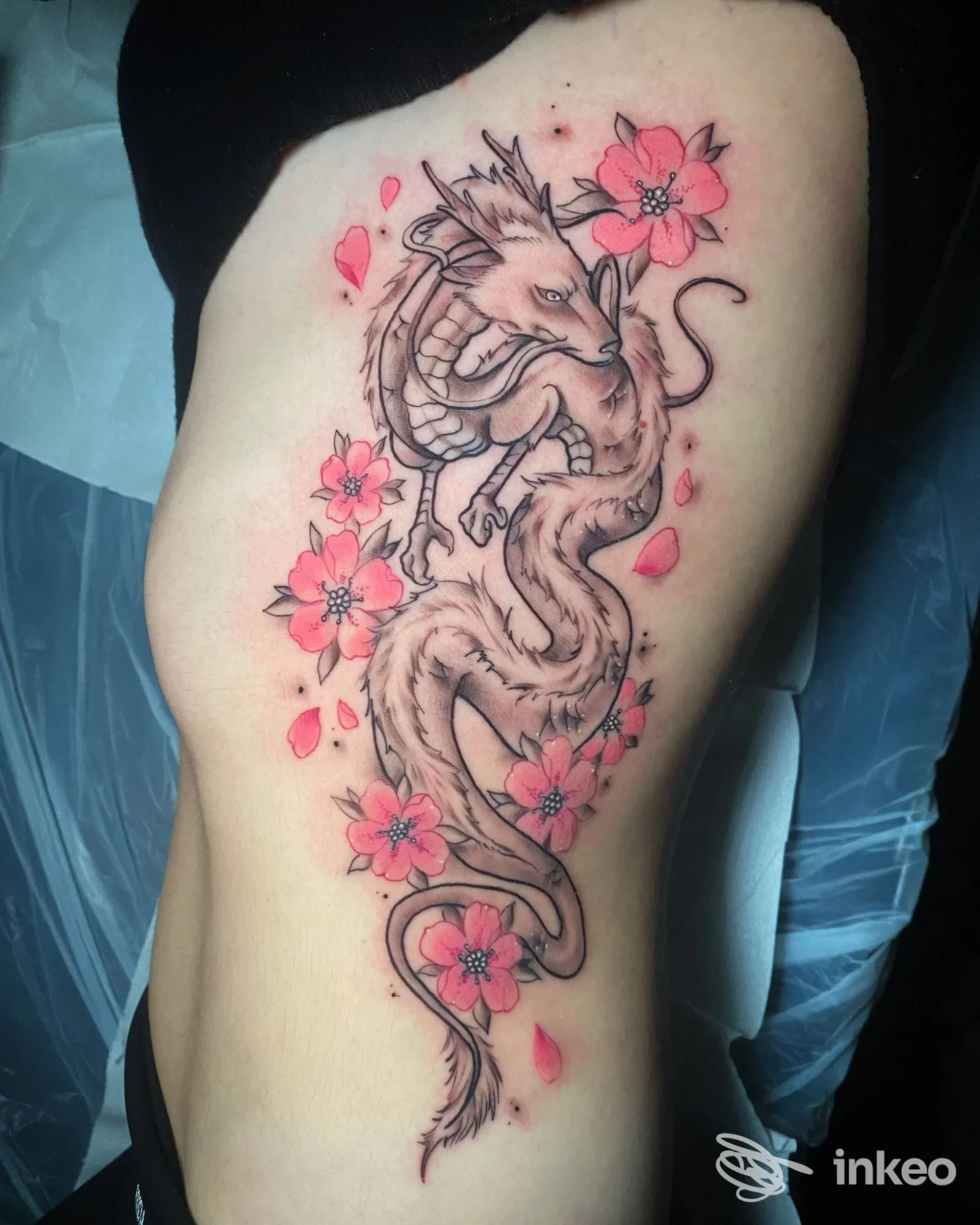 Tatuaggio a fianco con drago stilizzato e fiori rosa, eseguito da Soul Shop Tattoo Riccione a Riccione.