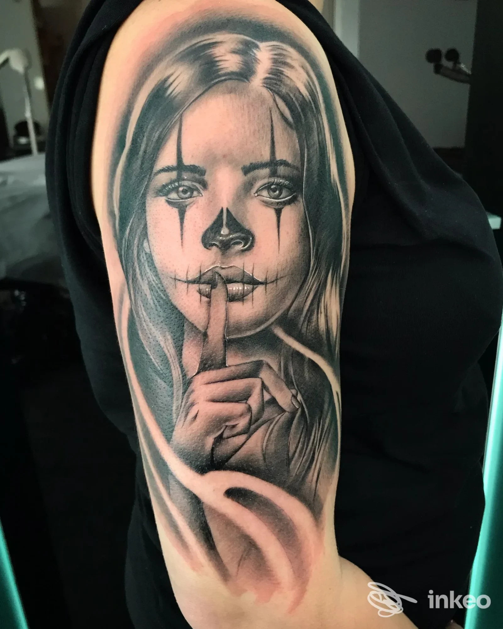 Tatuaggio bianco e nero sul braccio: volto femminile in stile clown con dito sulle labbra. Soul Shop Tattoo, Riccione.